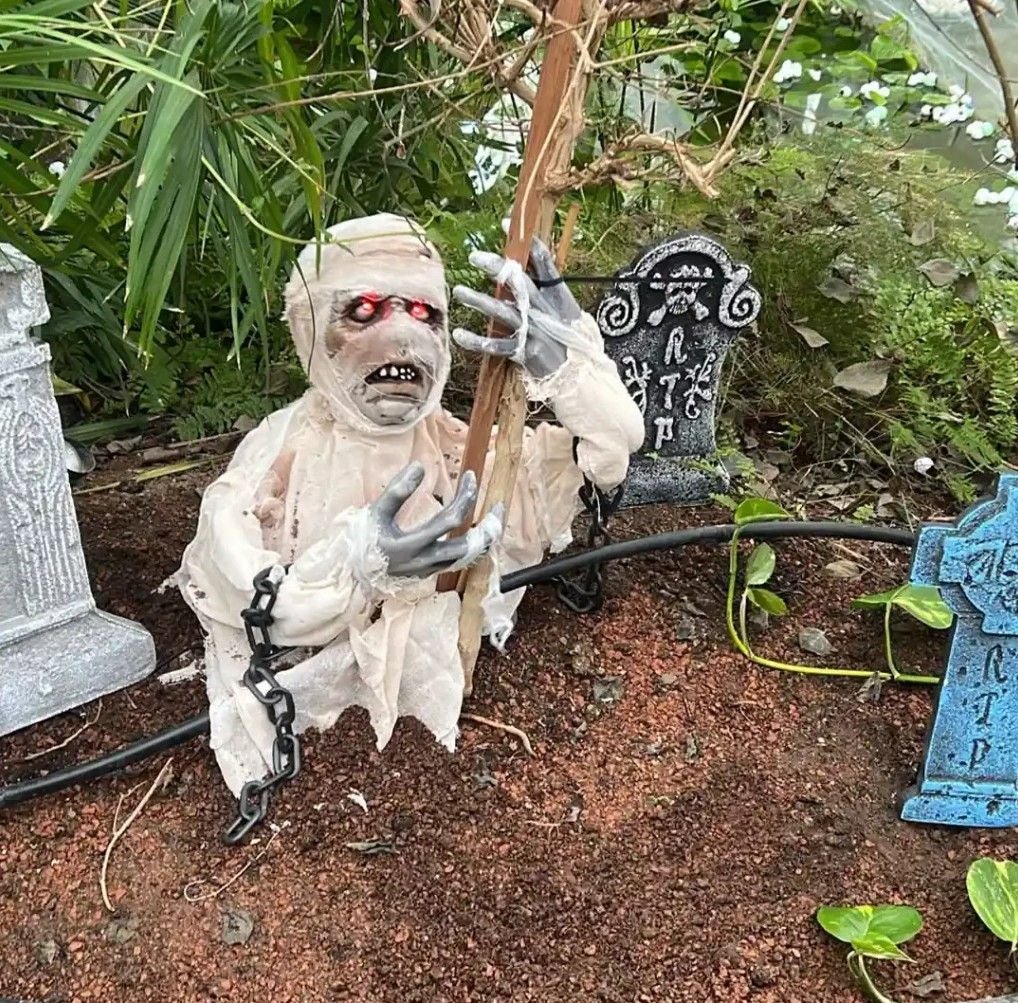 Halloween-Dekoration mit Mumie, leuchtenden roten Augen und Grabsteinen im Gruselgarten.