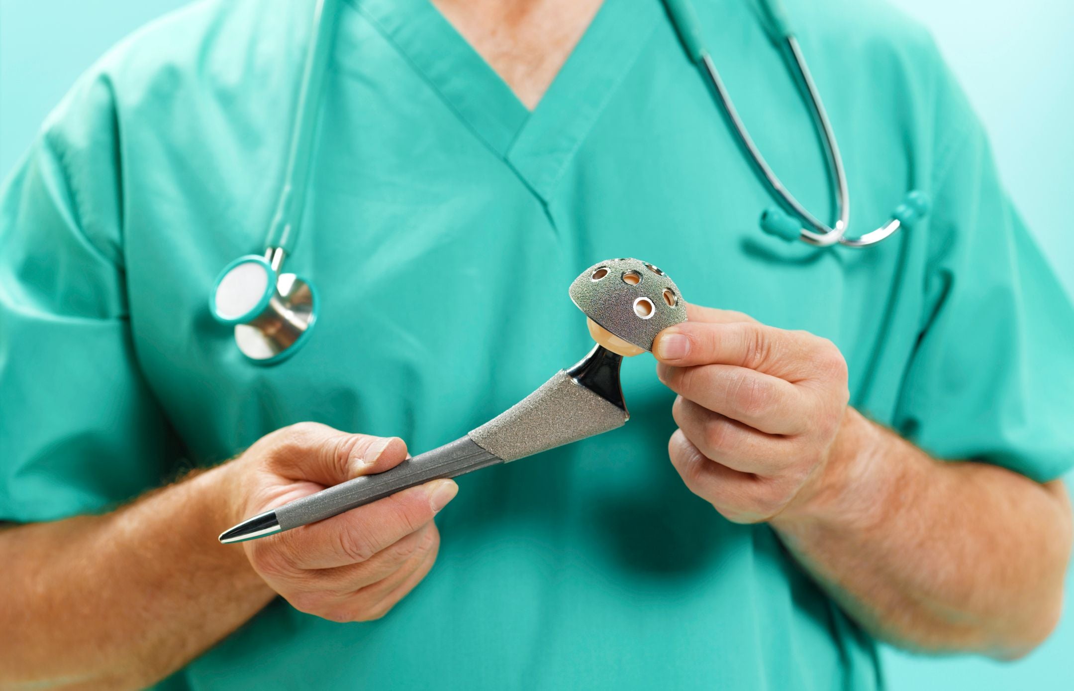 Orthopäde hält eine künstliche Hüftprothese in den Händen.