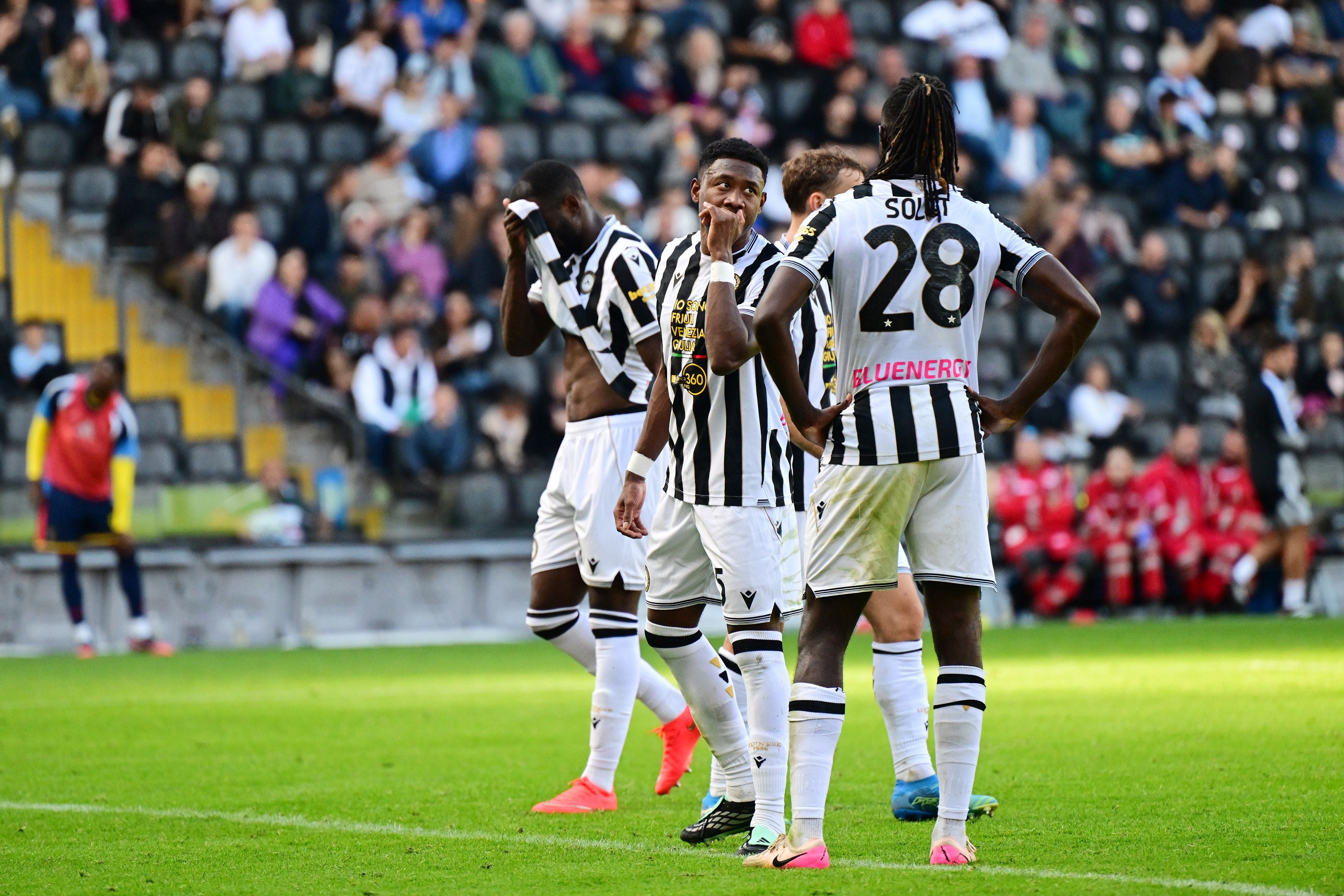 Mehrere Udinese-Spieler im schwarz-weißen Trikot stehen nachdenklich auf dem Fußballfeld.