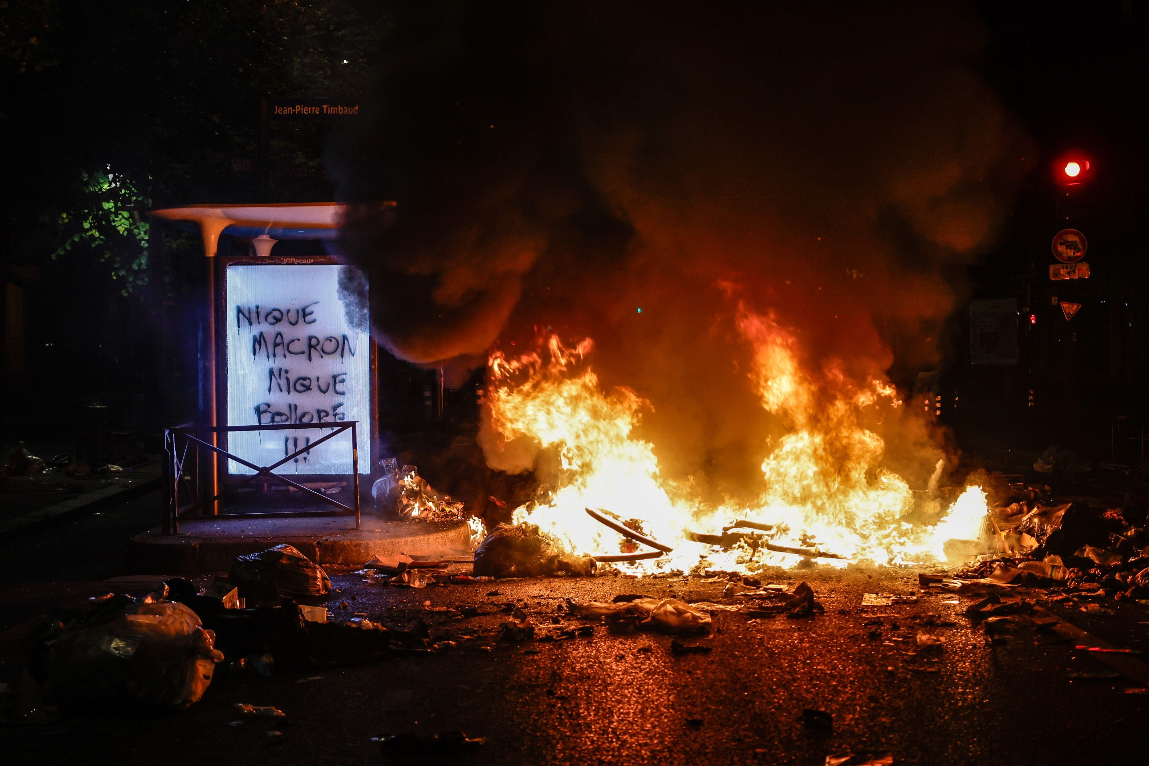 Brennende Straßensperre bei Protesten nachts in Paris, mit Rauch und Graffiti im Hintergrund.