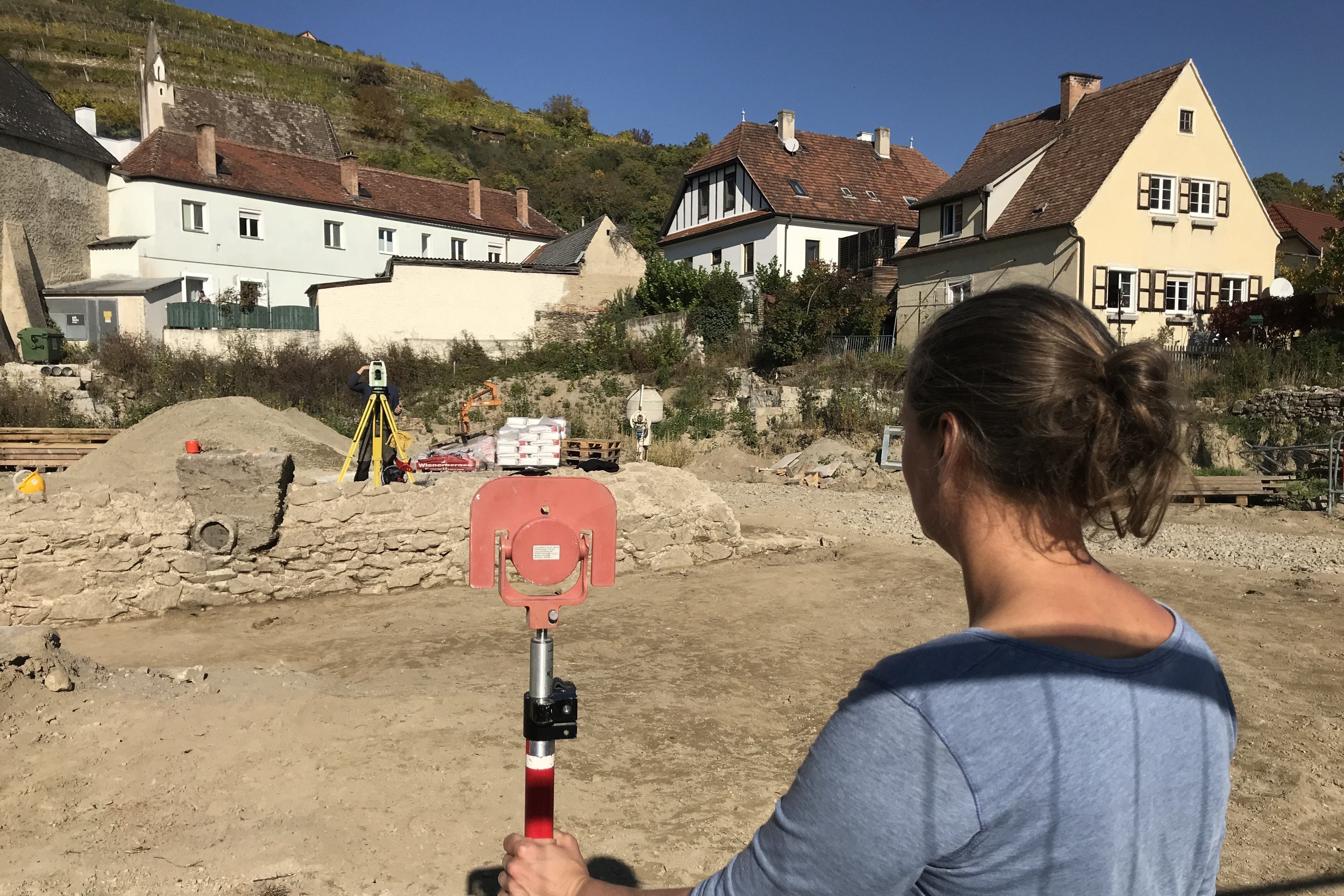 Eine Frau hält ein Vermessungsgerät auf einer Baustelle vor historischen Häusern in Förthof.