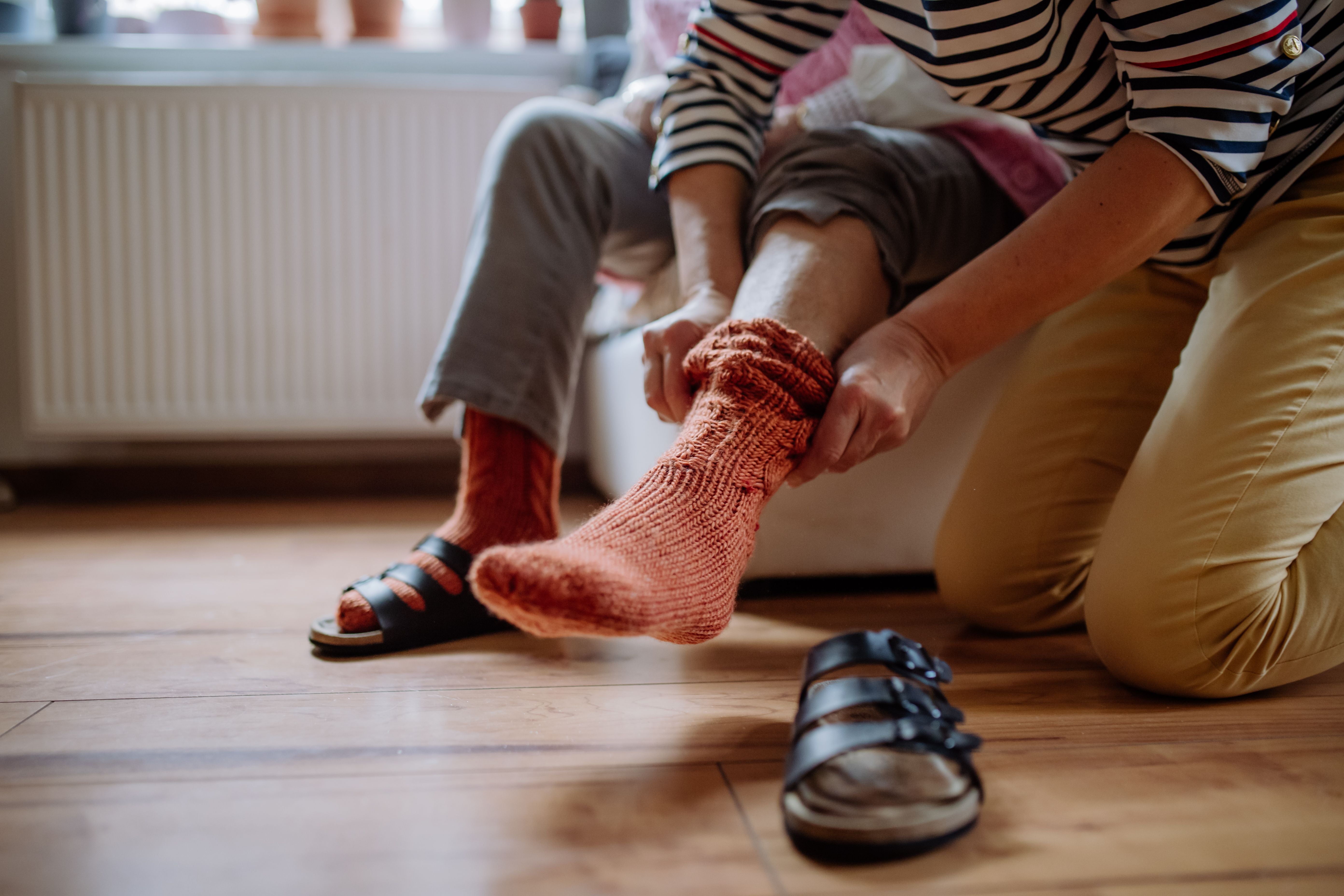 Ältere Frau erhält Hilfe beim Anziehen roter Socken von einer Pflegekraft.