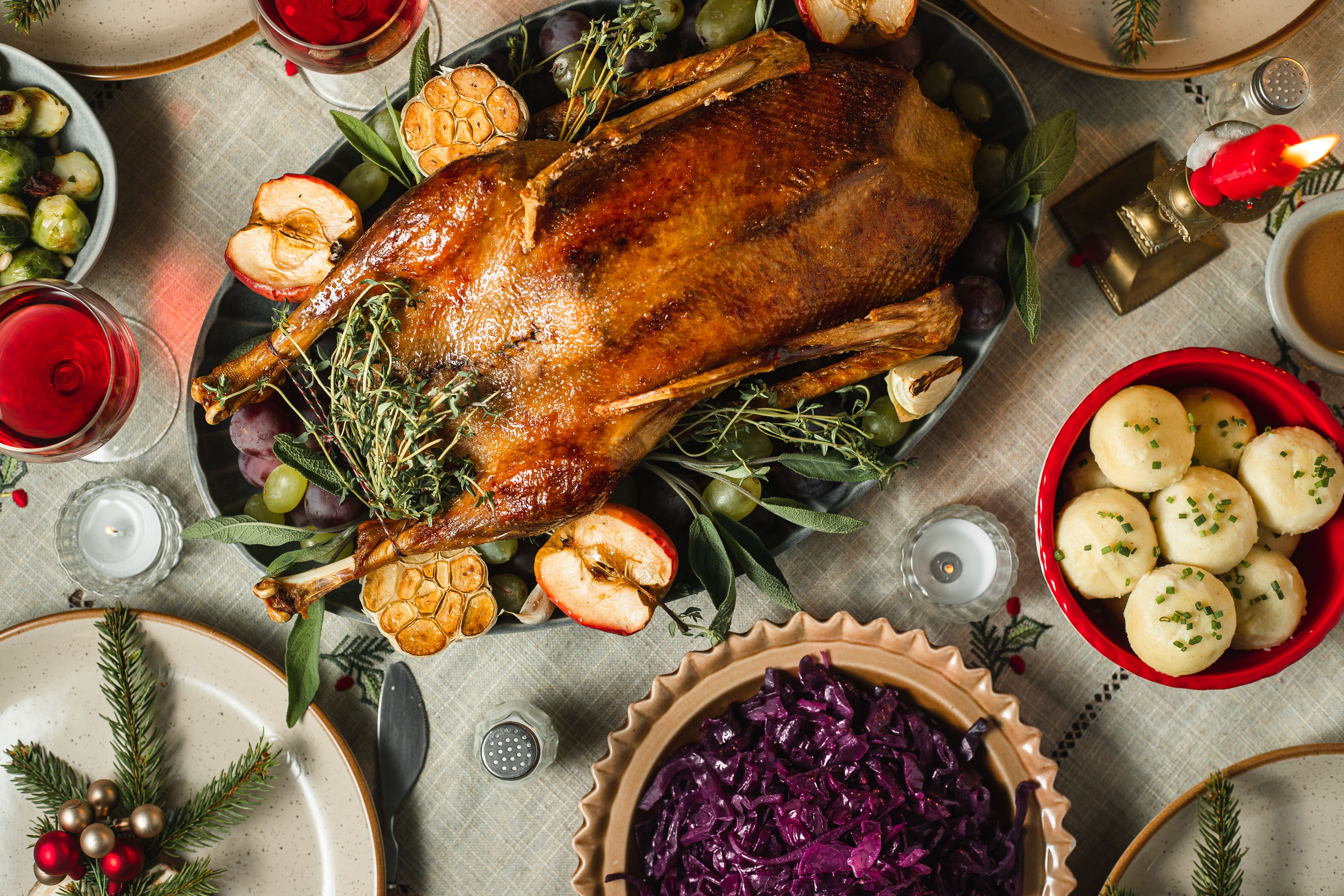 Festlich gedeckter Tisch mit gebratener Gans, Rotkohl, Knödel und Dekoration.