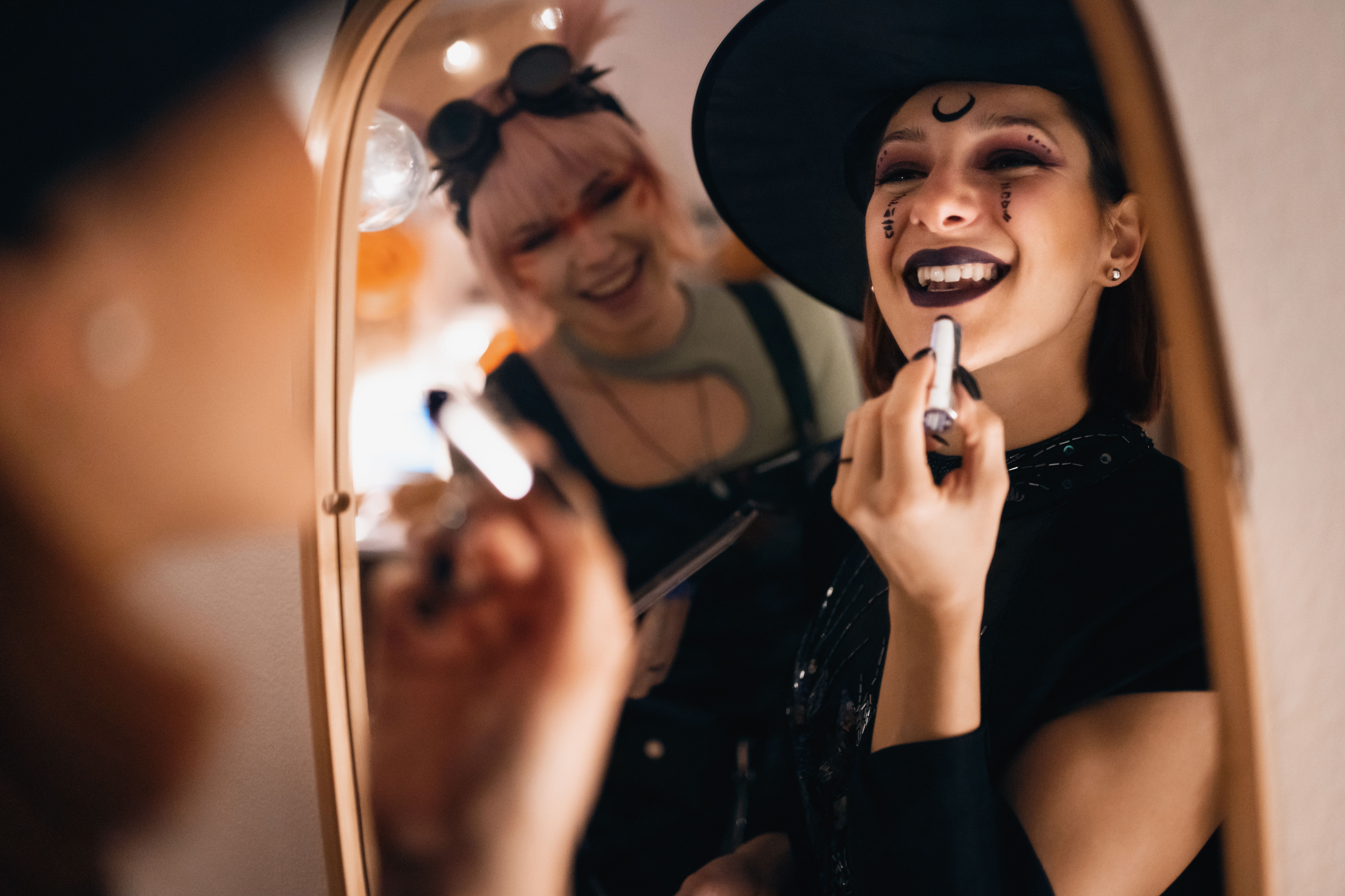 Zwei Freundinnen schminken sich verkleidet im Spiegel für eine Halloween-Party.