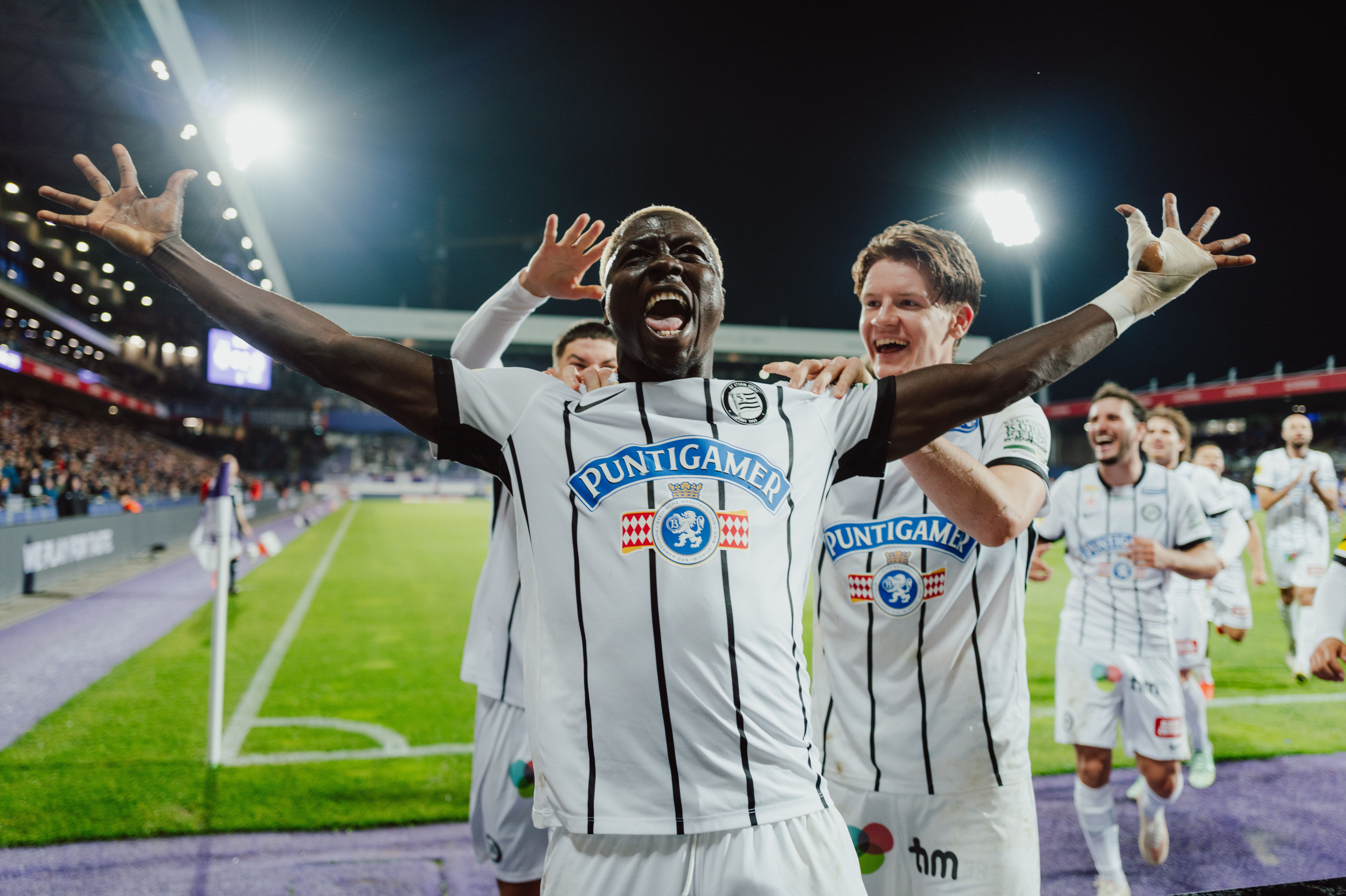 Fußballspieler von Sturm Graz jubeln auf dem Spielfeld nach einem Tor bei Nacht.
