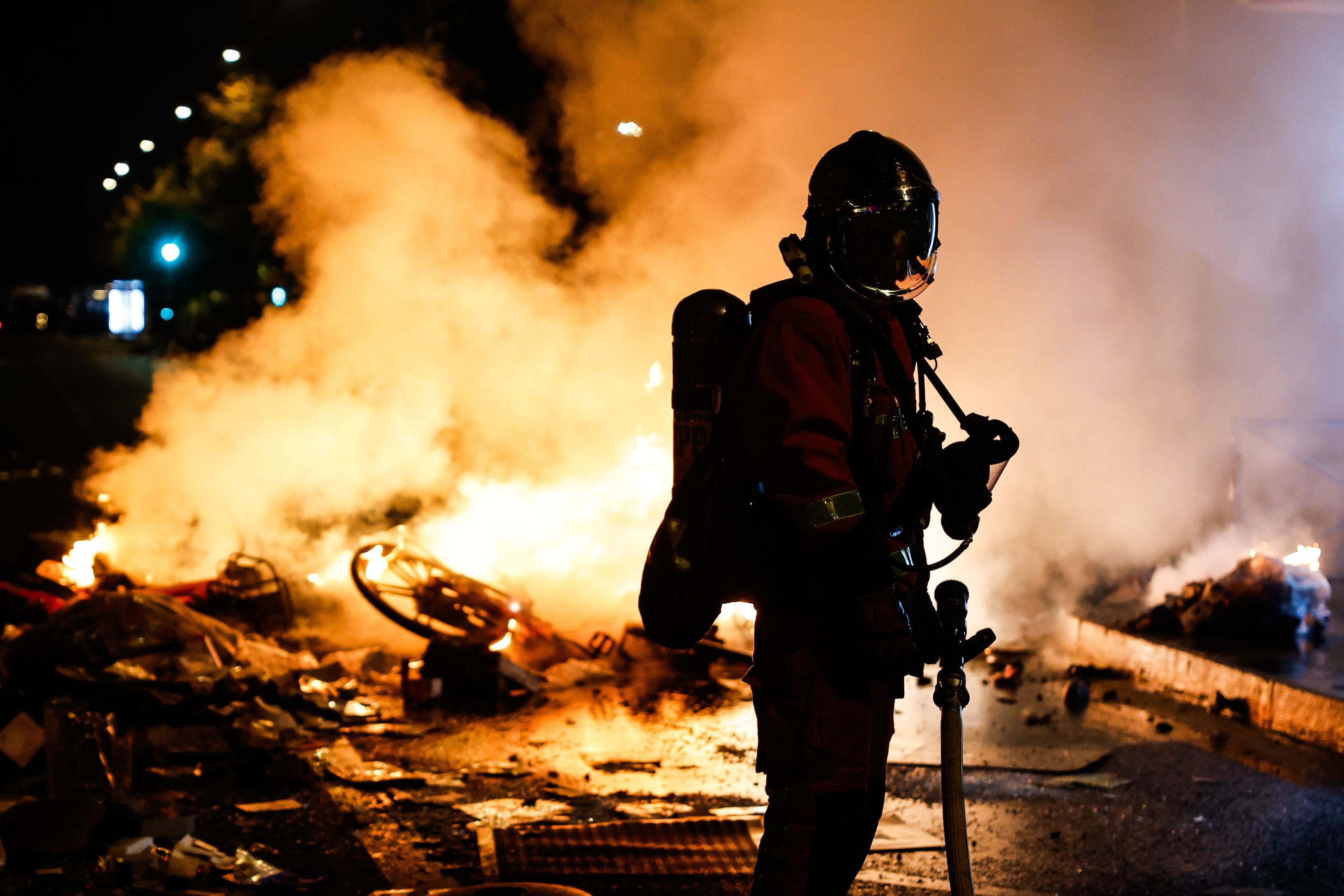 Ein Feuerwehrmann steht mit Ausrüstung vor einer brennenden Barrikade und dichtem Rauch auf der Straße.