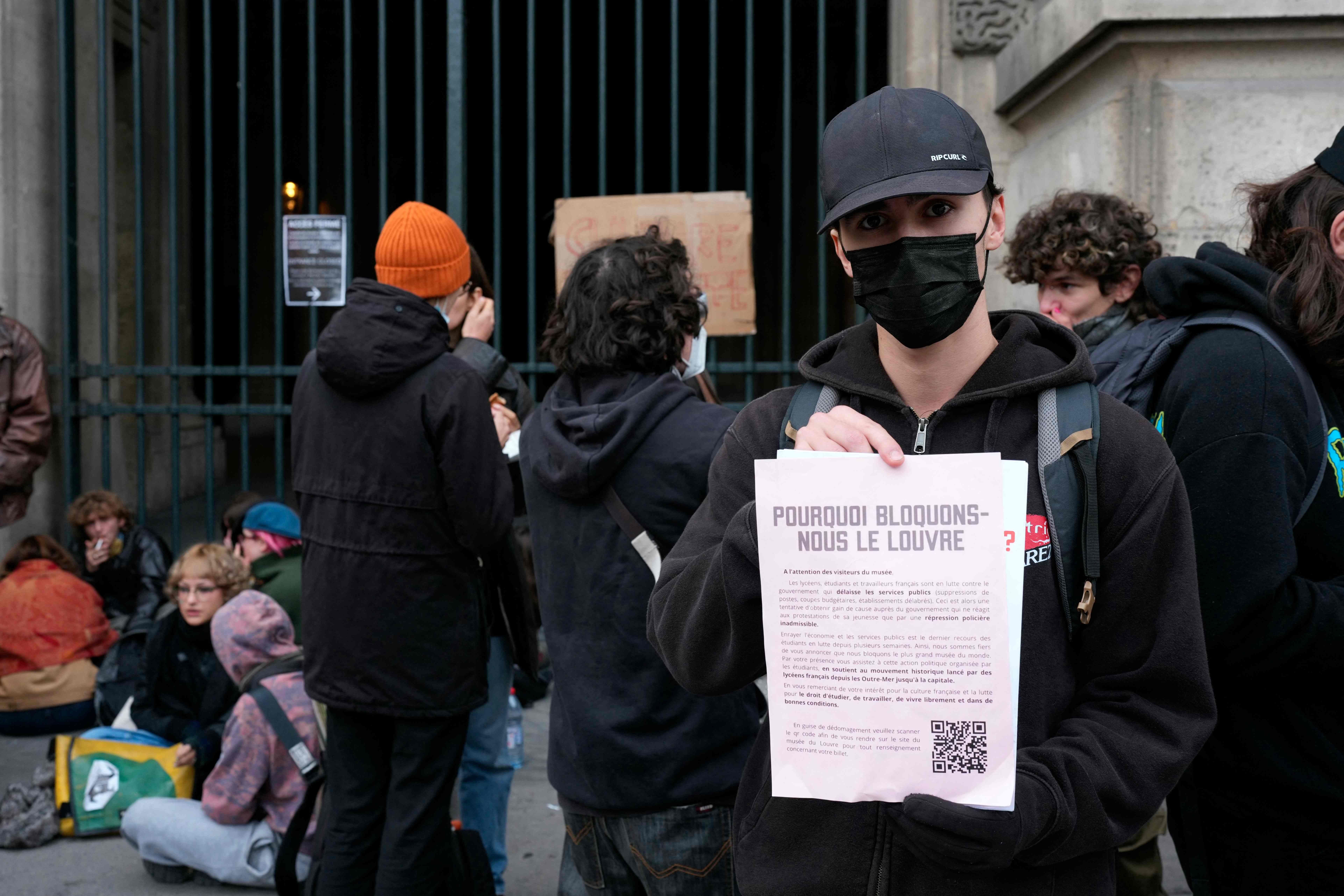 Ein Jugendlicher hält ein Flugblatt vor dem Louvre, während Protestierende den Eingang blockieren.