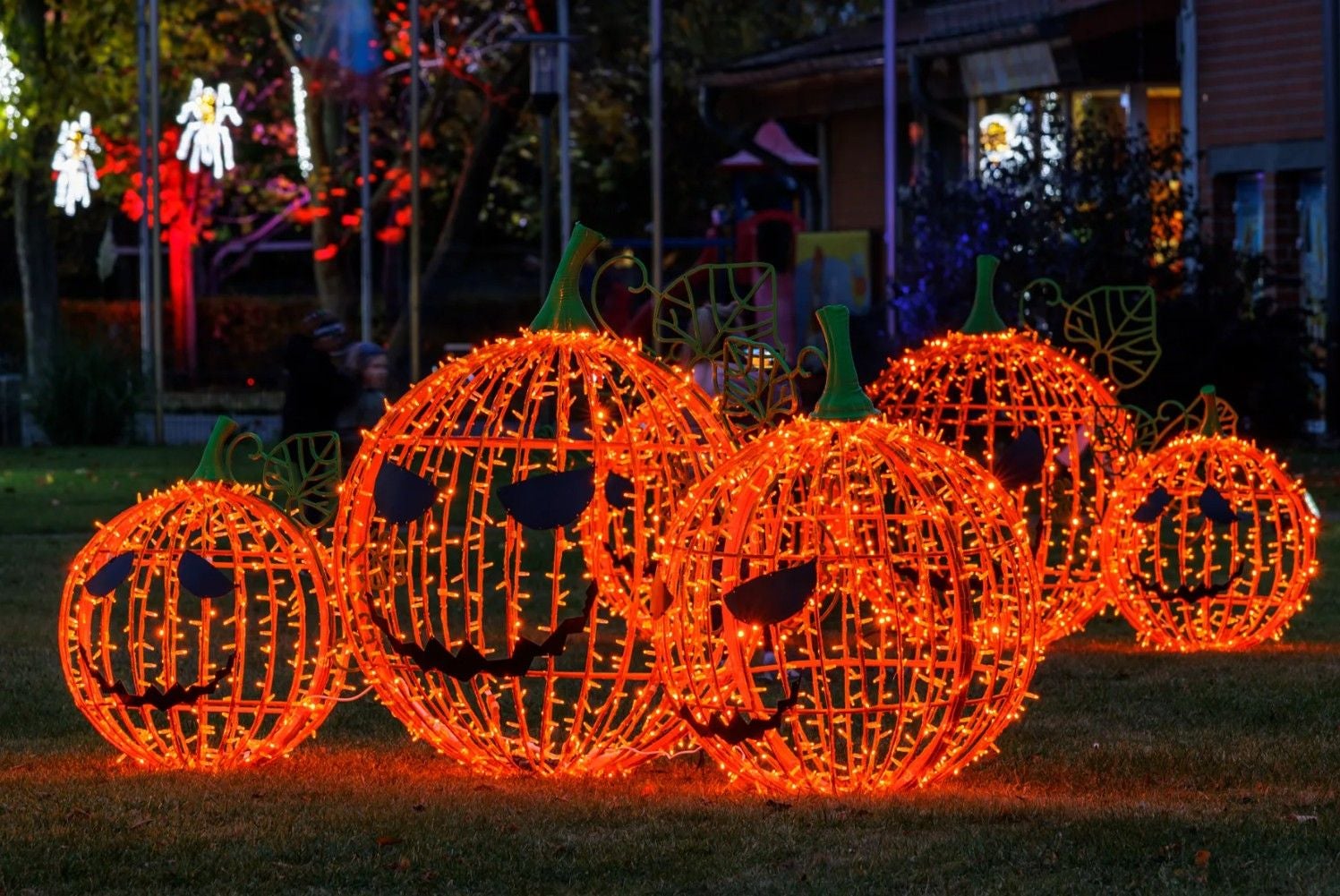 Leuchtende Kürbisfiguren mit Lichterketten bei einer Halloween-Dekoration im Freien.