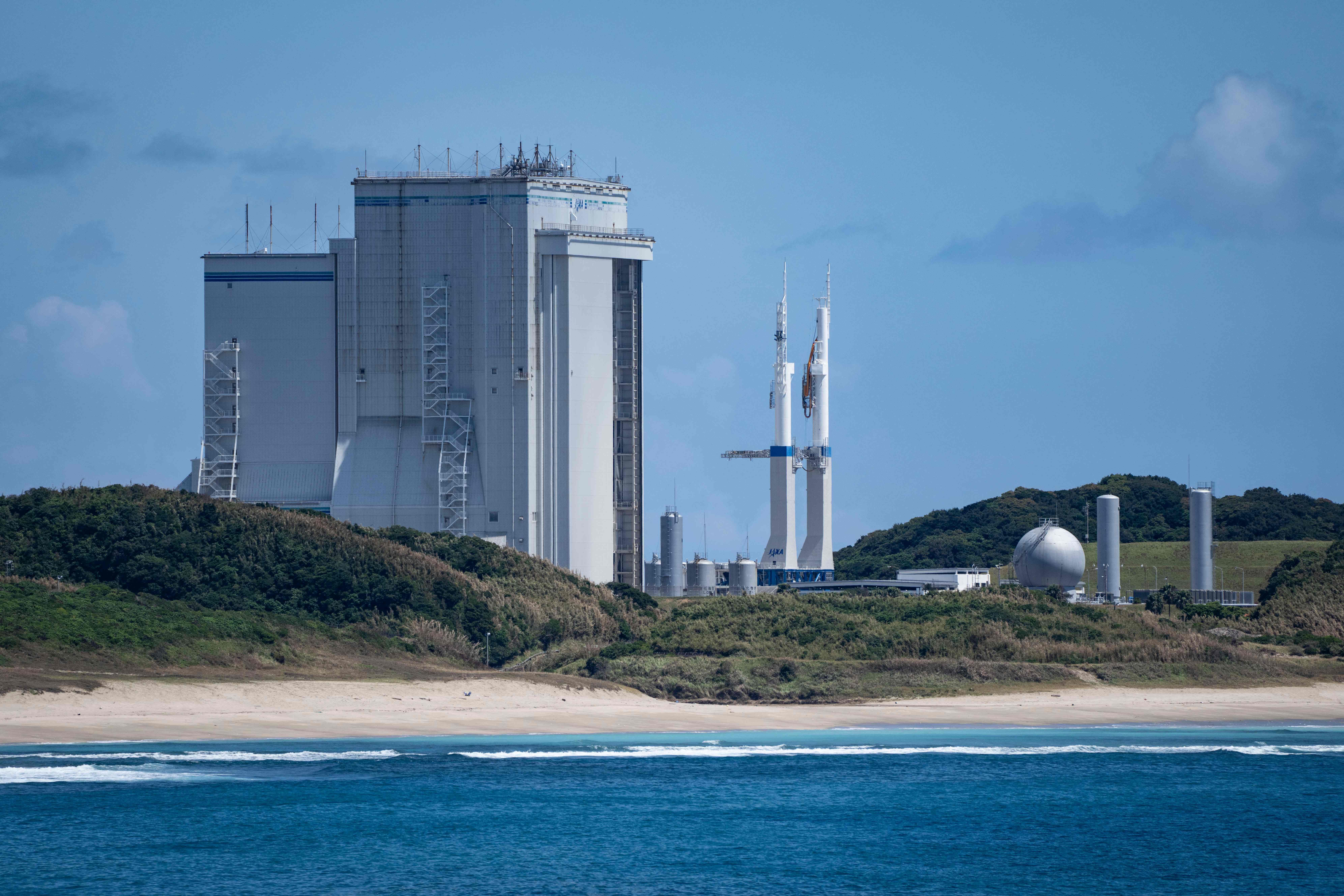 Das Tanegashima Space Center mit Raketenstartsilo und Gebäuden am Meer unter blauem Himmel.