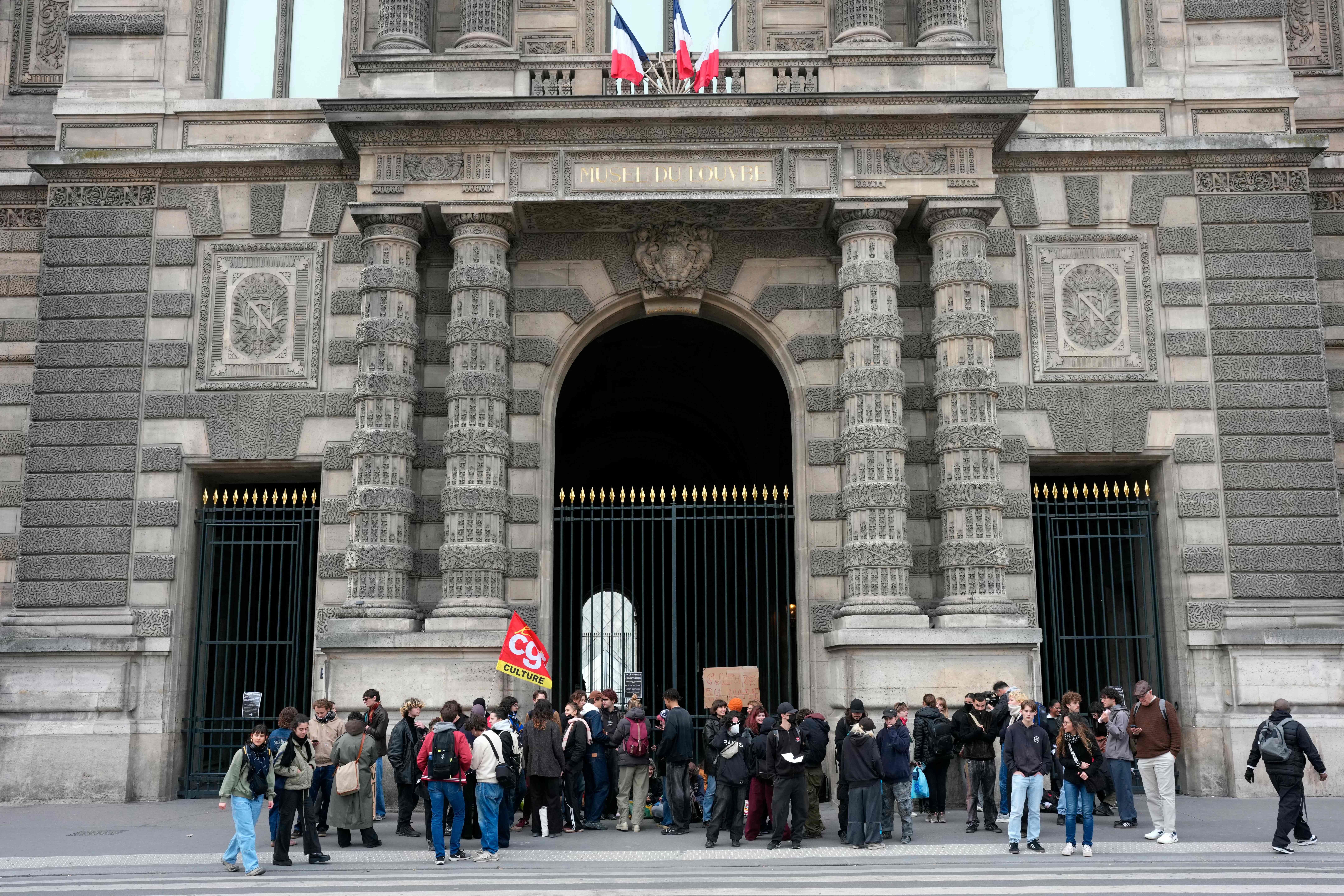 Demonstranten blockieren einen Eingang des Louvre-Museums in Paris und halten eine rot-gelbe Fahne.