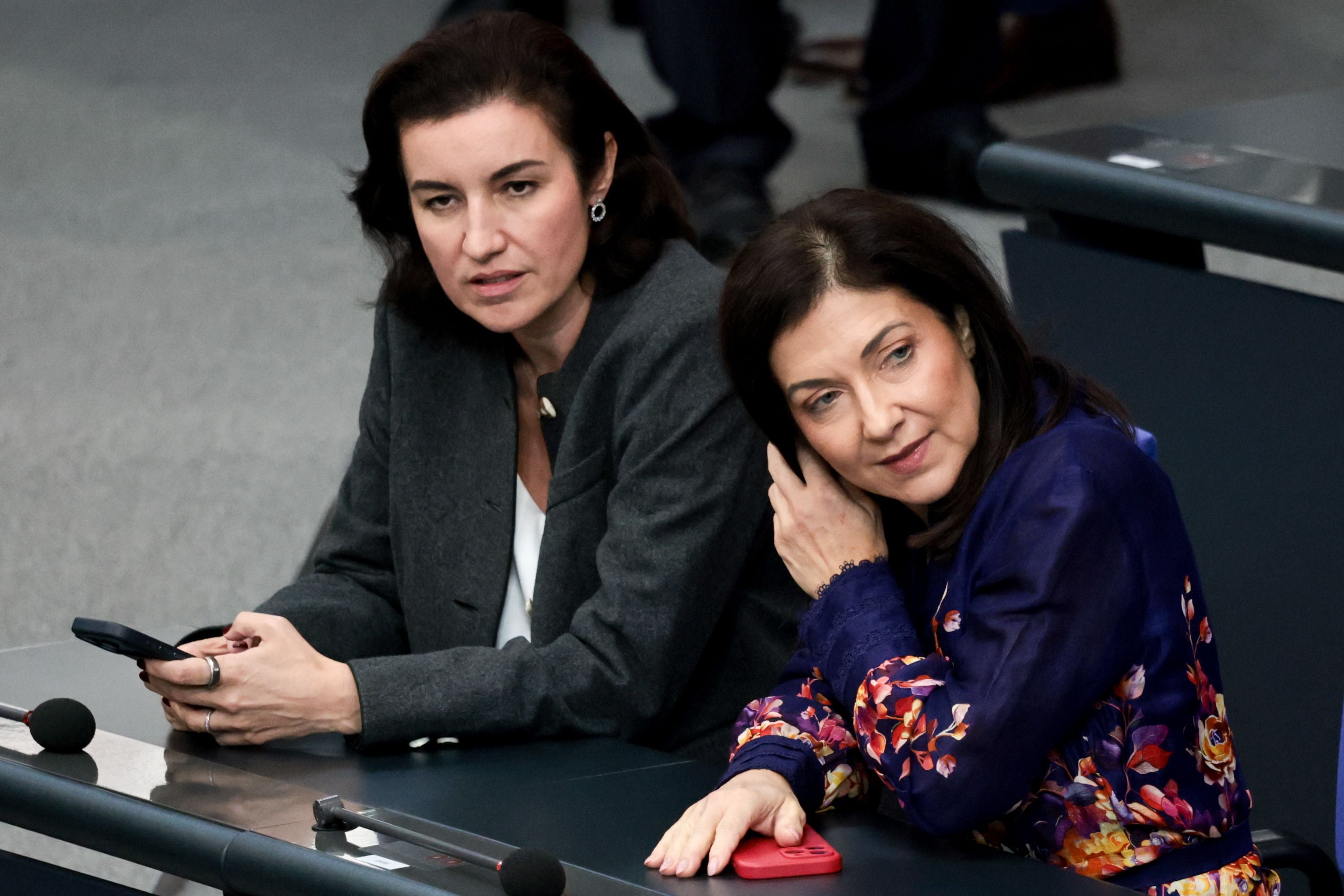 Zwei Frauen sitzen nebeneinander im Bundestag, beide mit Smartphones in den Händen.