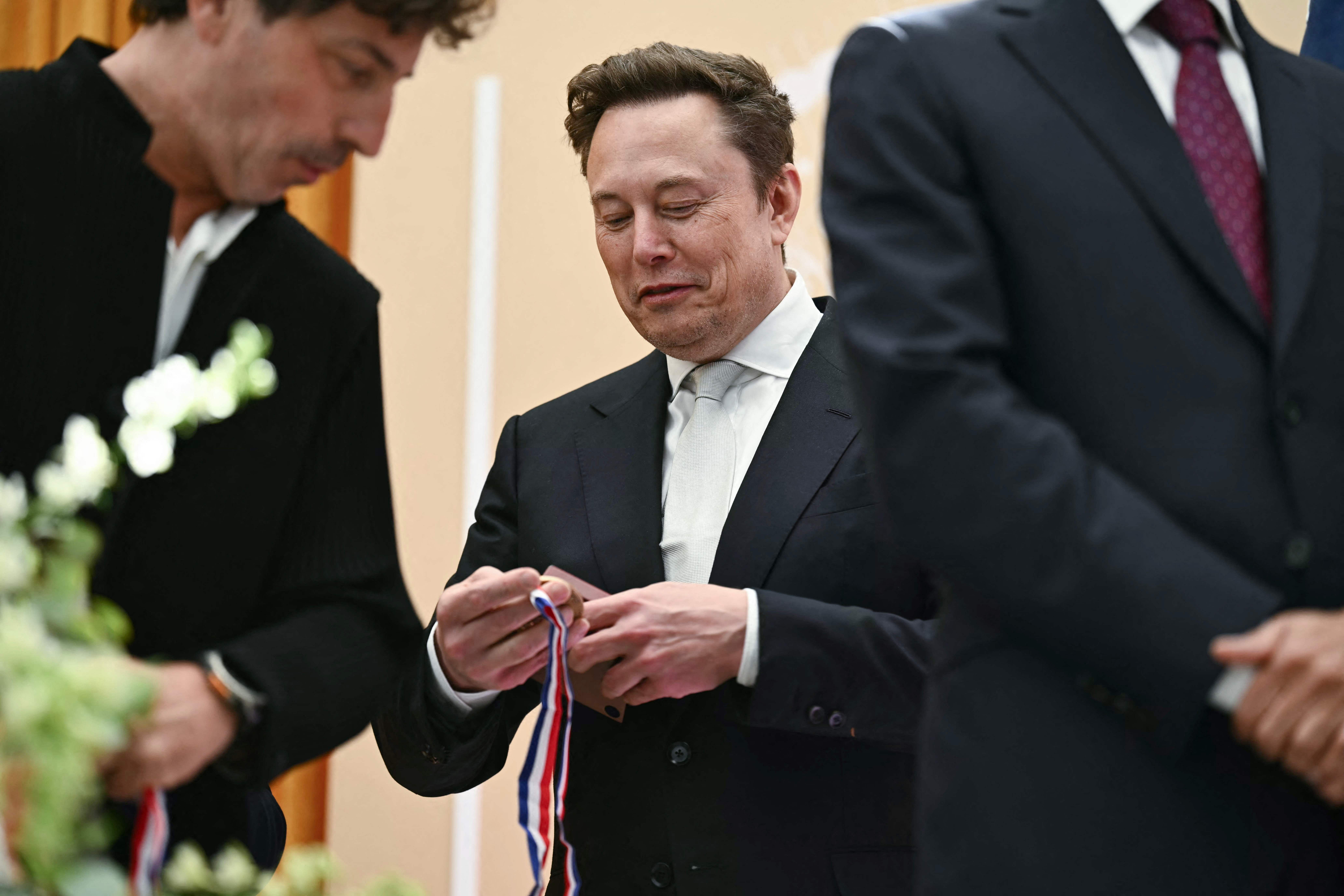 Elon Musk hält eine Medaille während einer Preisverleihung in einem formellen Rahmen.