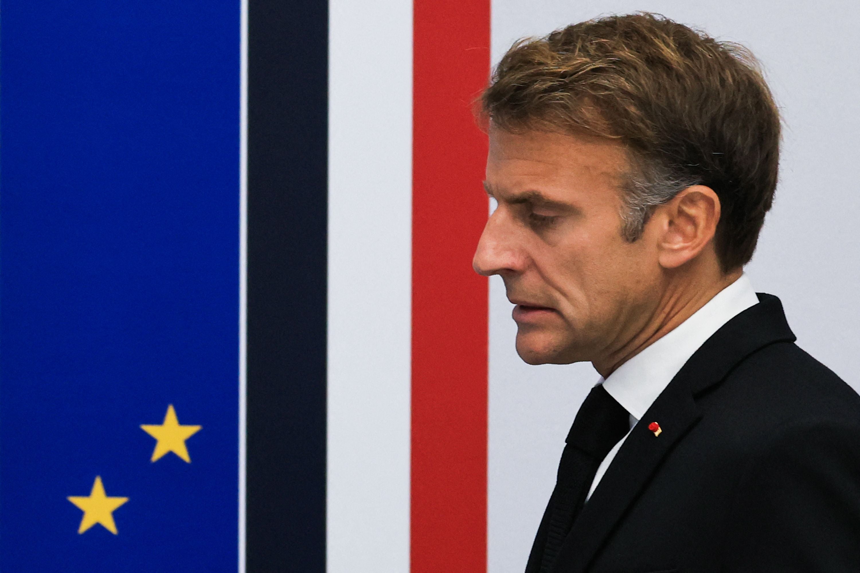 Ein Mann im Anzug steht nachdenklich vor einer Wand mit EU- und Frankreich-Farben.