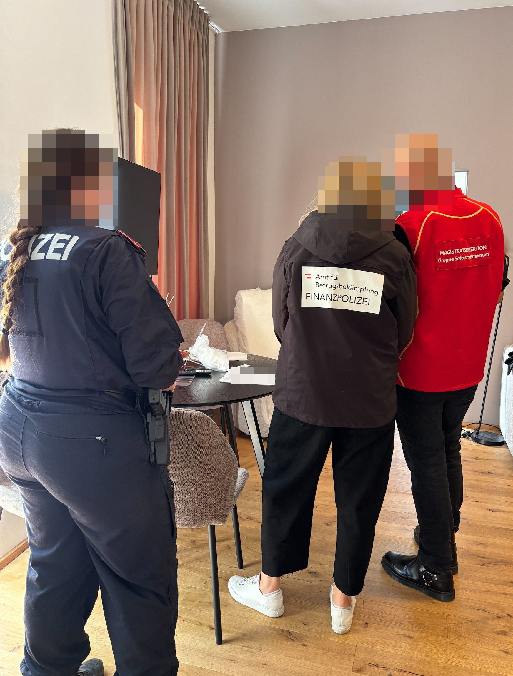 Drei Personen von Polizei, Finanzpolizei und Magistratsdirektion bei einer Kontrolle in einem Zimmer.