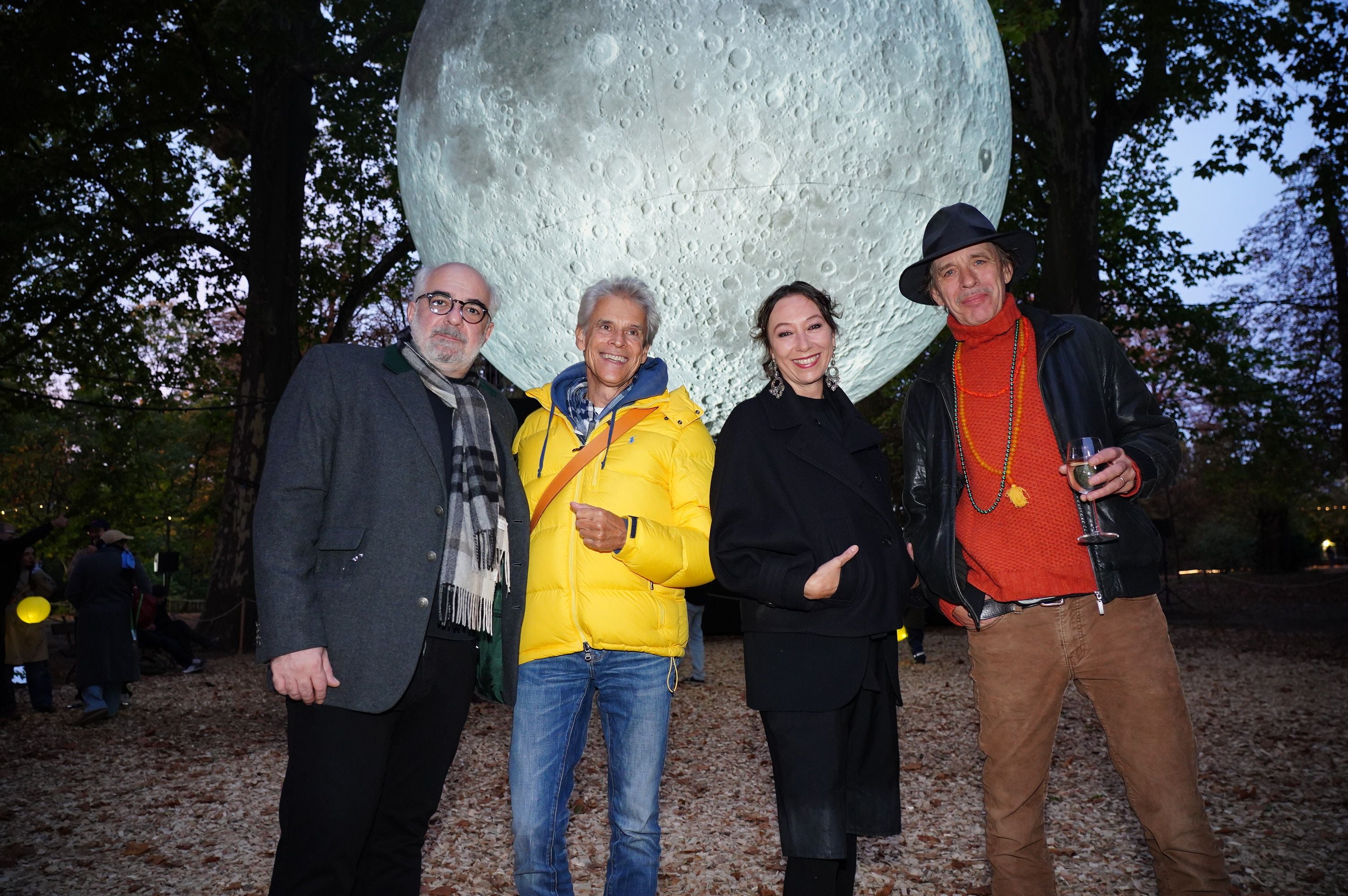 Vier Menschen posieren vor einer großen leuchtenden Mondinstallation im Park bei Abenddämmerung.