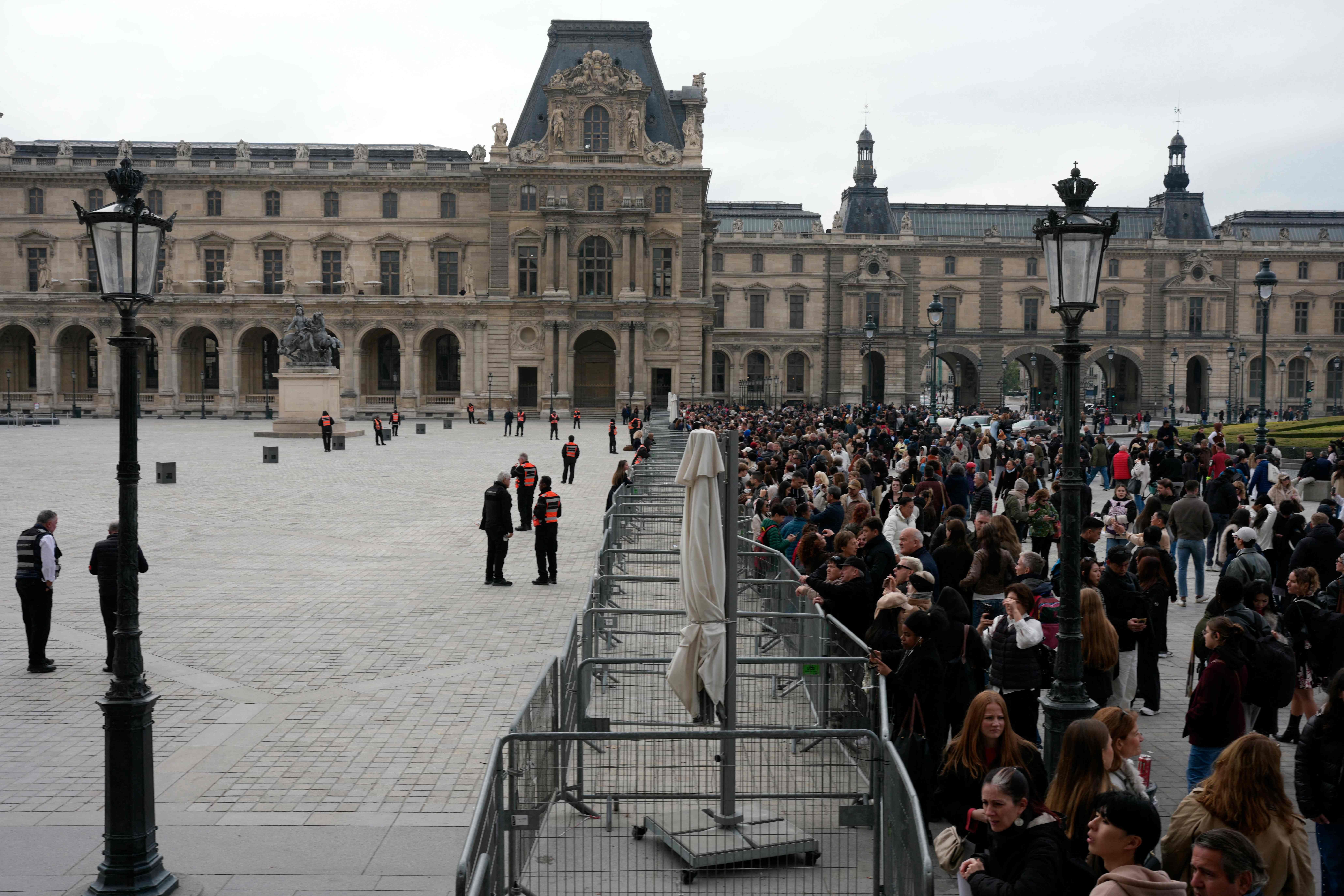 Menschenmenge steht vor dem Louvre-Museum, das durch Absperrungen und Sicherheitspersonal geschützt wird.