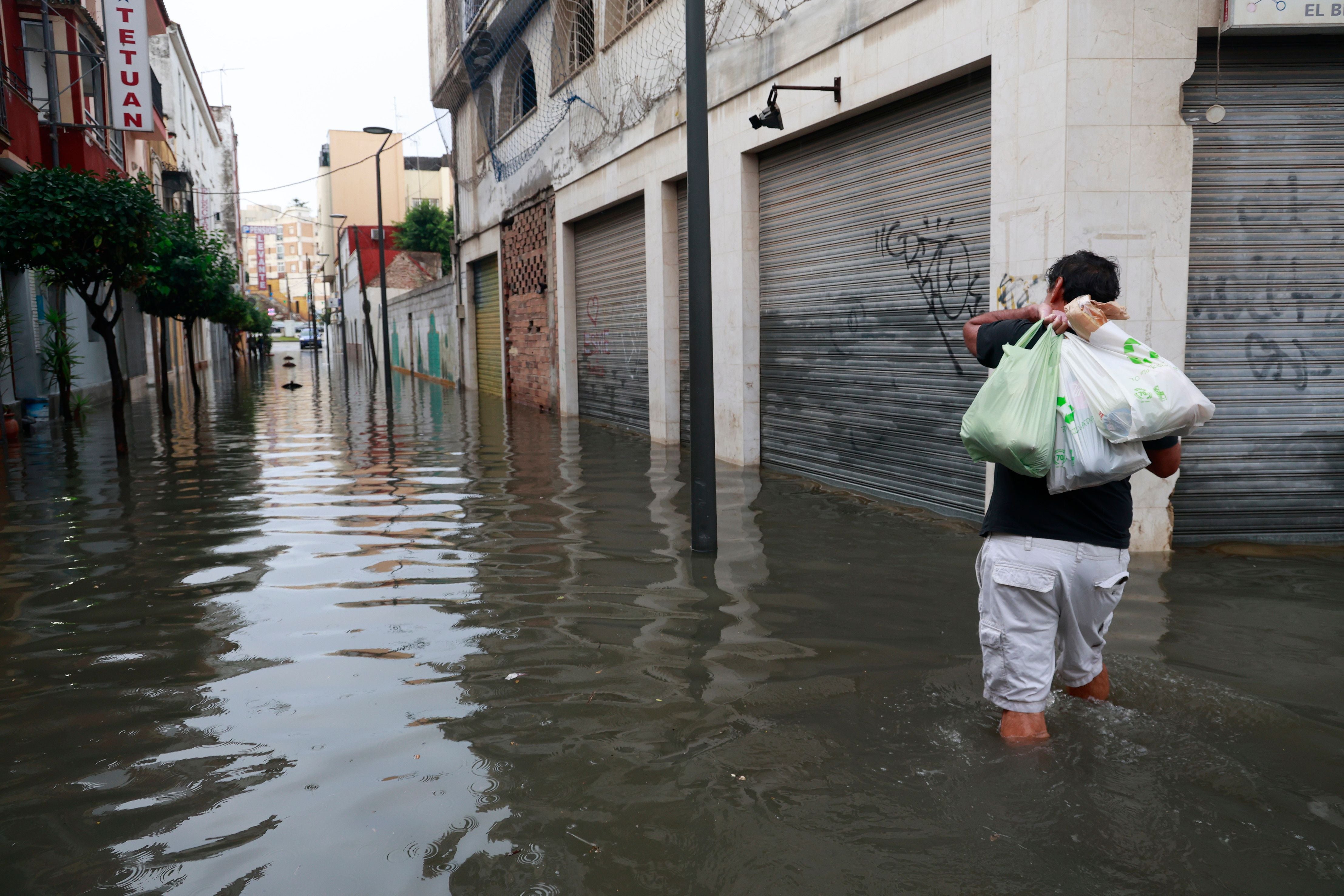 Eine Person watet mit Einkaufstüten durch eine überflutete Straße in Algeciras, Spanien.