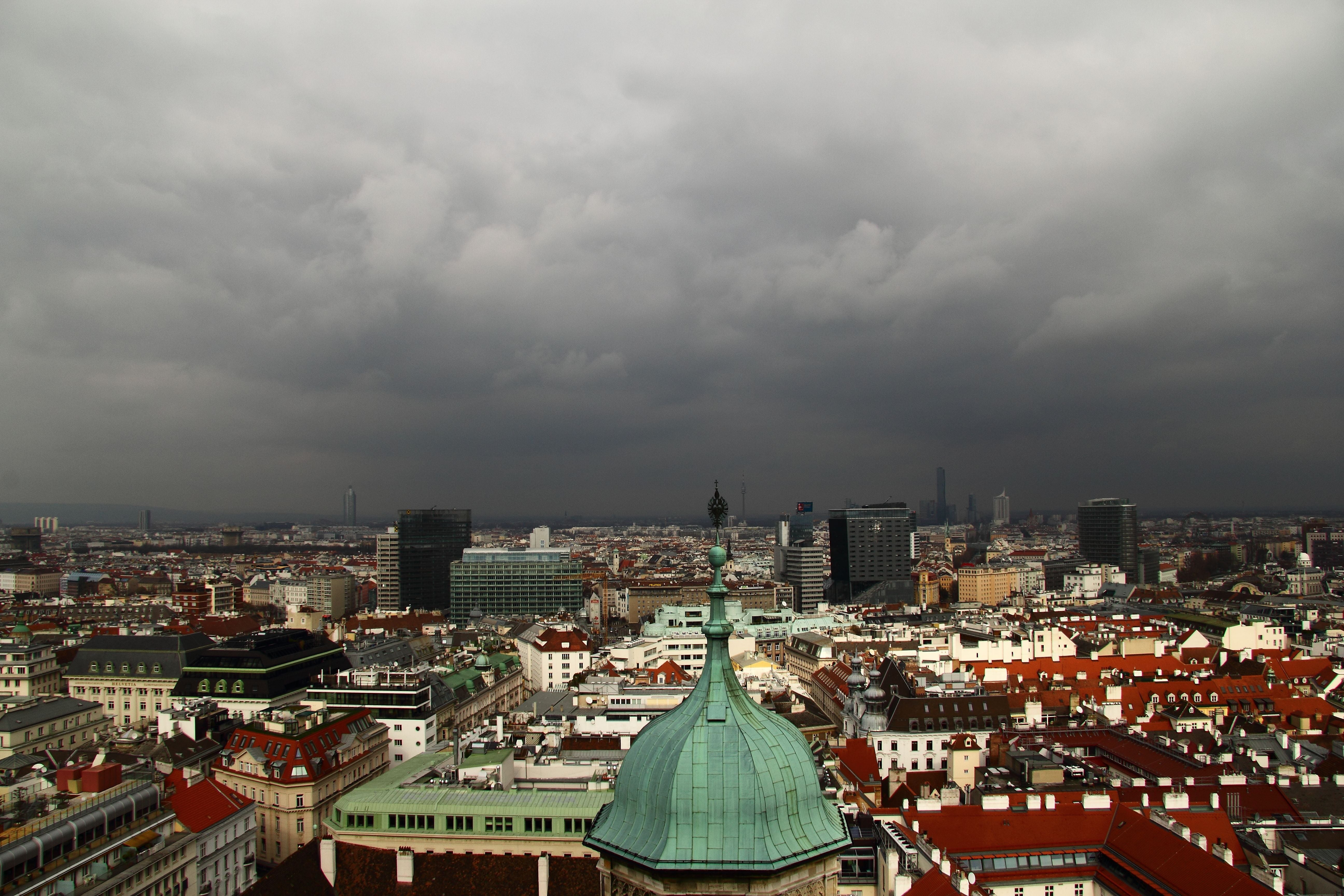 Panoramablick auf Wien mit dunklen Wolken über der Stadt und vielen roten Dächern im Vordergrund.