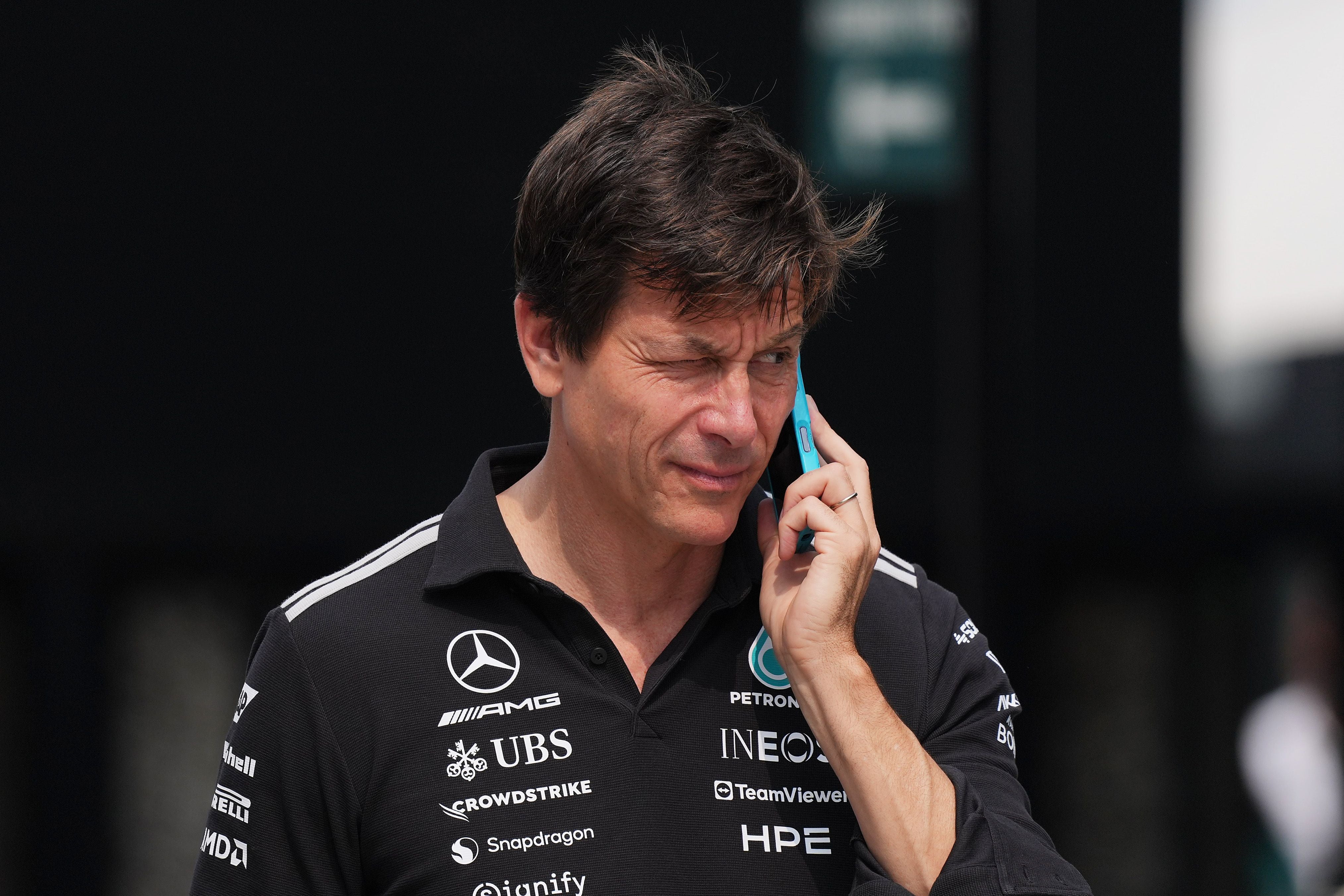 Ein Mann im Mercedes-AMG-Petronas-Shirt telefoniert im Freien und blinzelt in die Sonne.