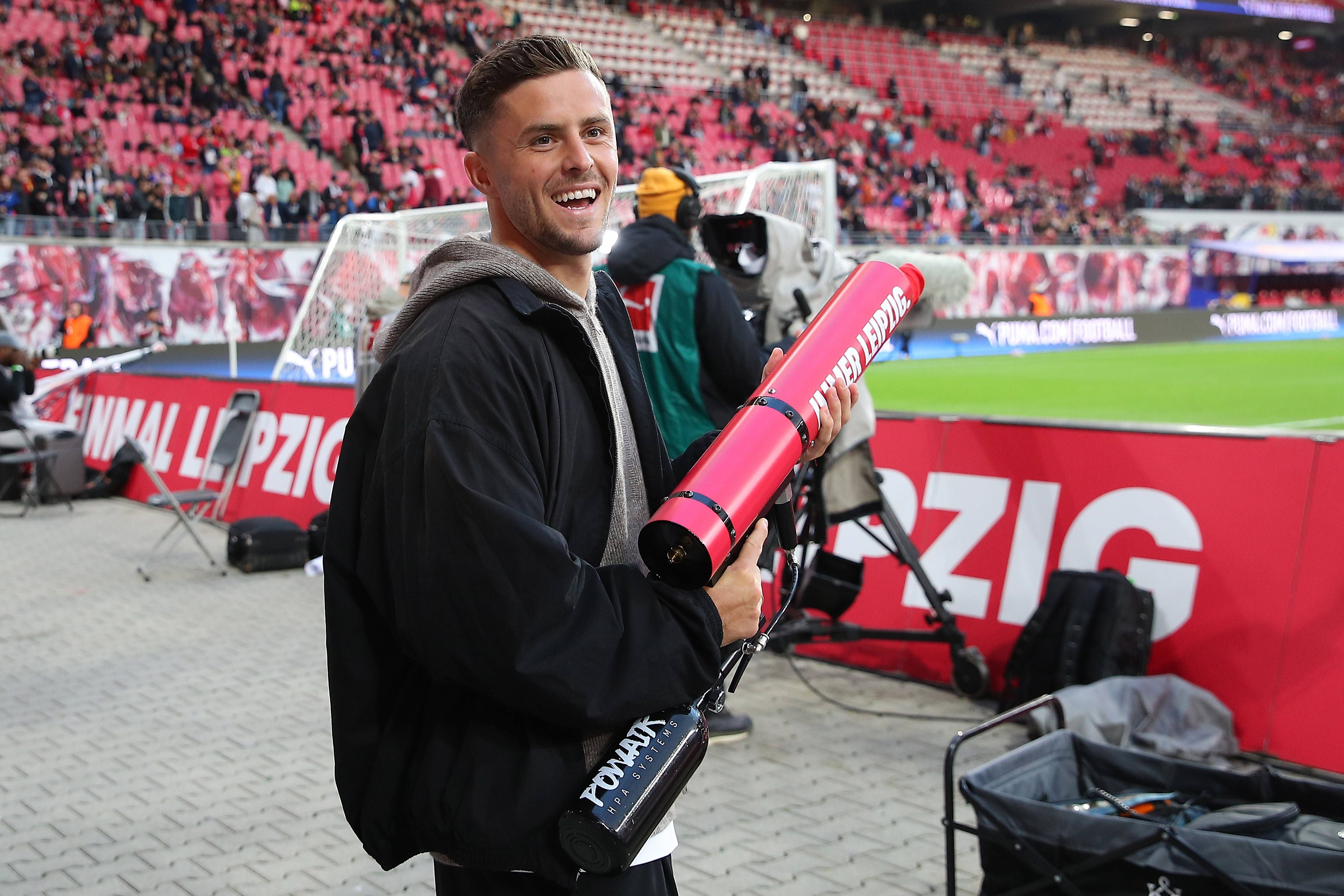 Ein Mann steht im Stadion und hält eine T-Shirt-Kanone, im Hintergrund Zuschauerränge.