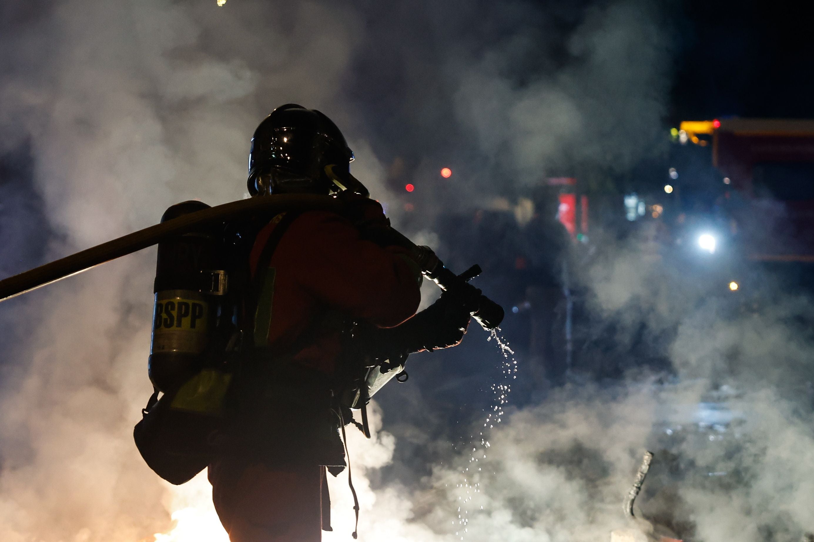 Ein Feuerwehrmann löscht nachts brennende Barrikaden im dichten Rauch auf einer Straße.