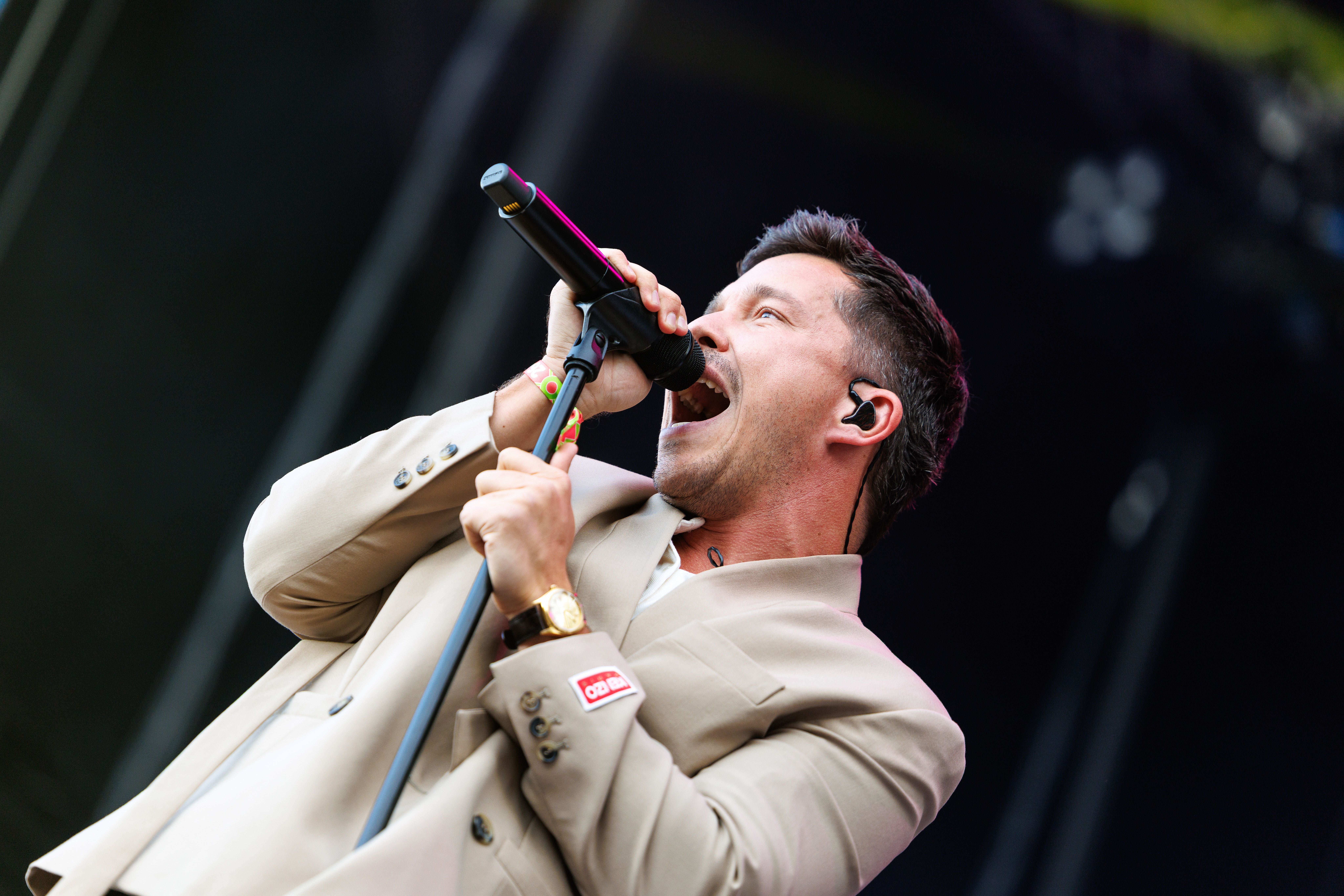 Nico Santos im beigem Anzug singt leidenschaftlich in ein Mikrofon auf einer Bühne.