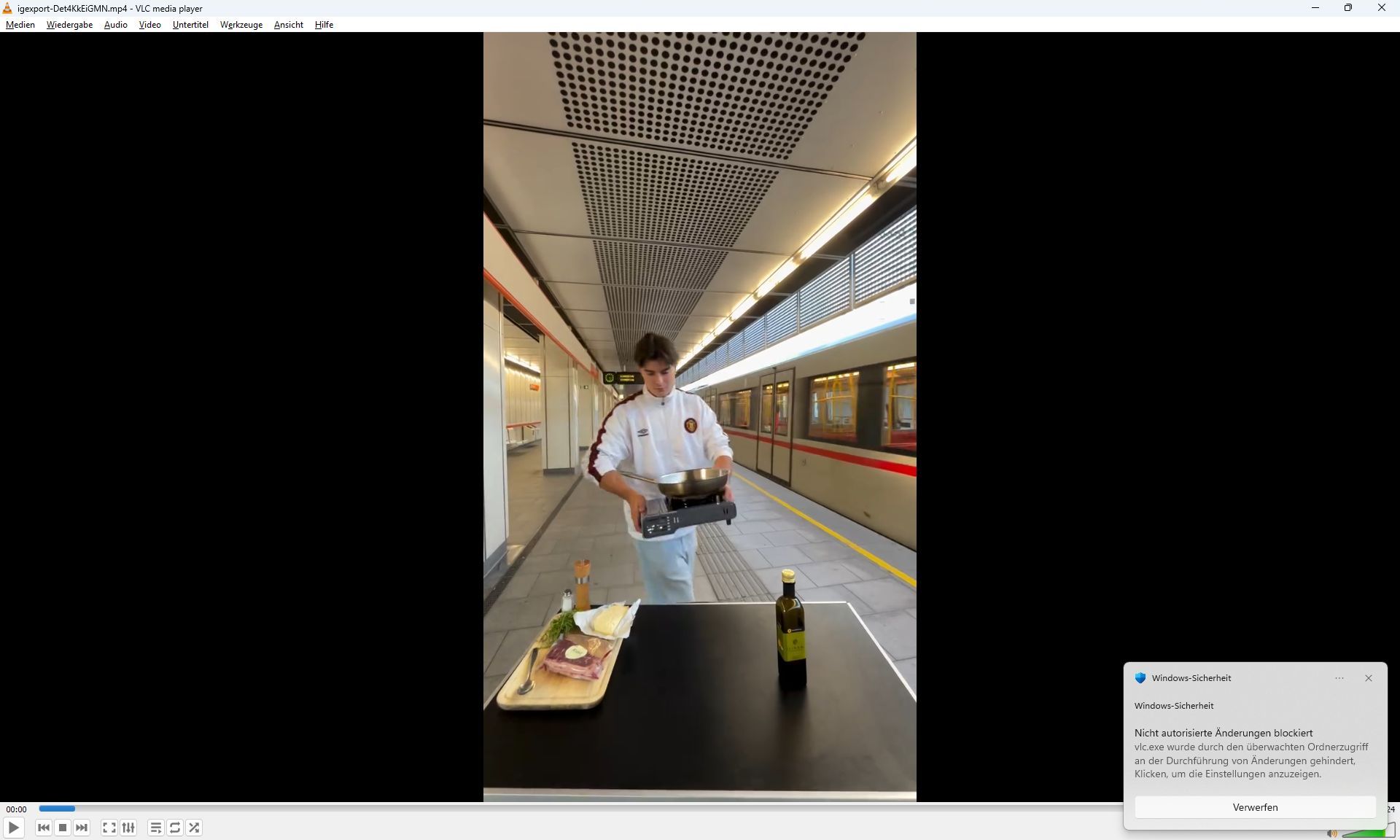 Ein Mann steht mit einer Pfanne auf einem Bahnsteig, vor ihm liegt Steakzubehör auf einem Tisch.