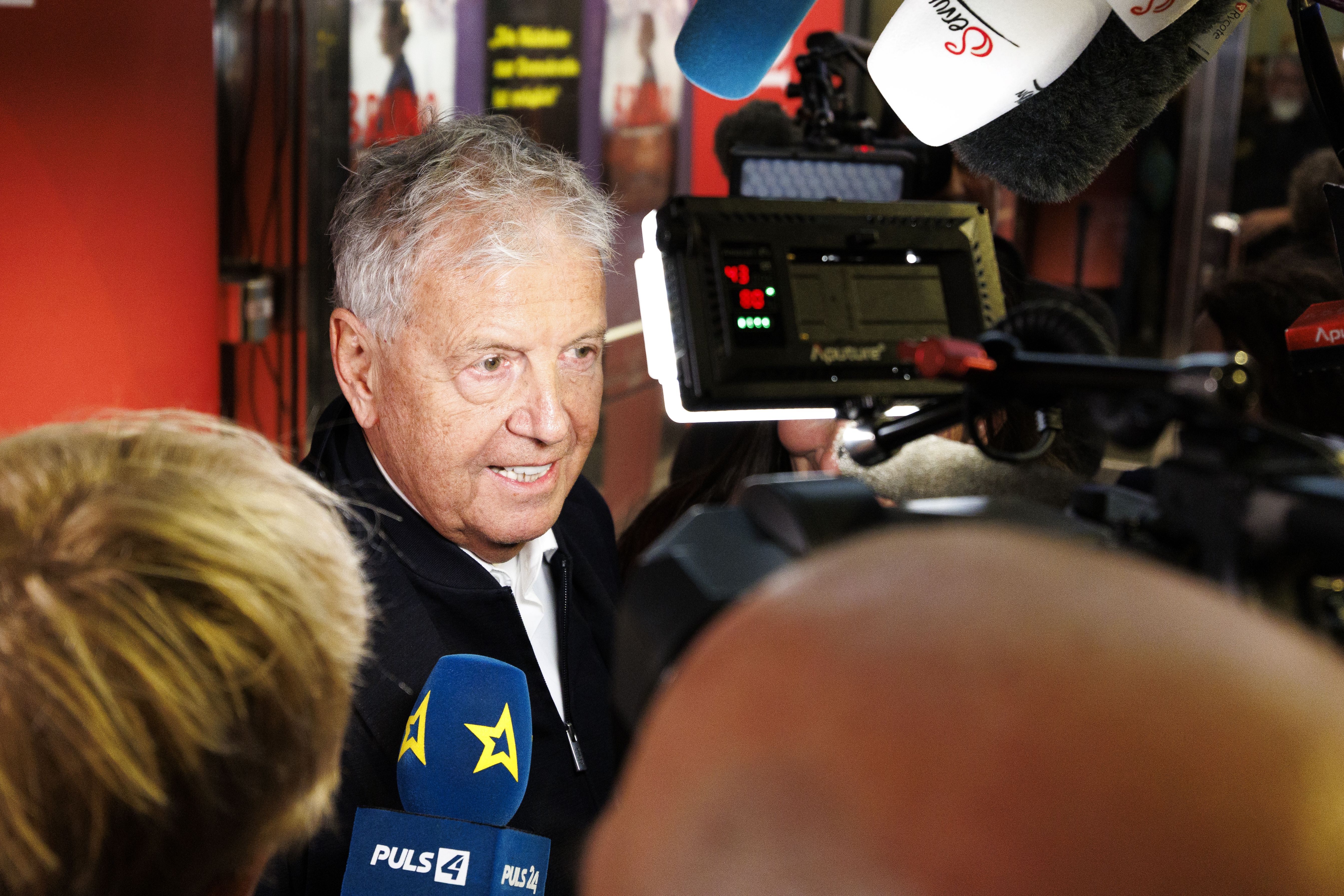Ein älterer Mann wird bei einer Filmpremiere von mehreren Mikrofonen und Kameras interviewt.
