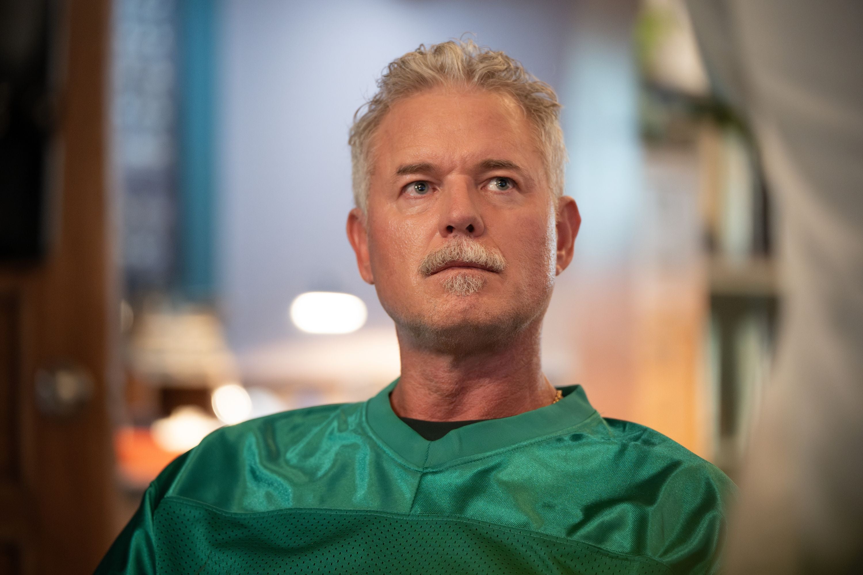 Mittelalterlicher Mann mit grauen Haaren im grünen Shirt blickt ernst nach oben.