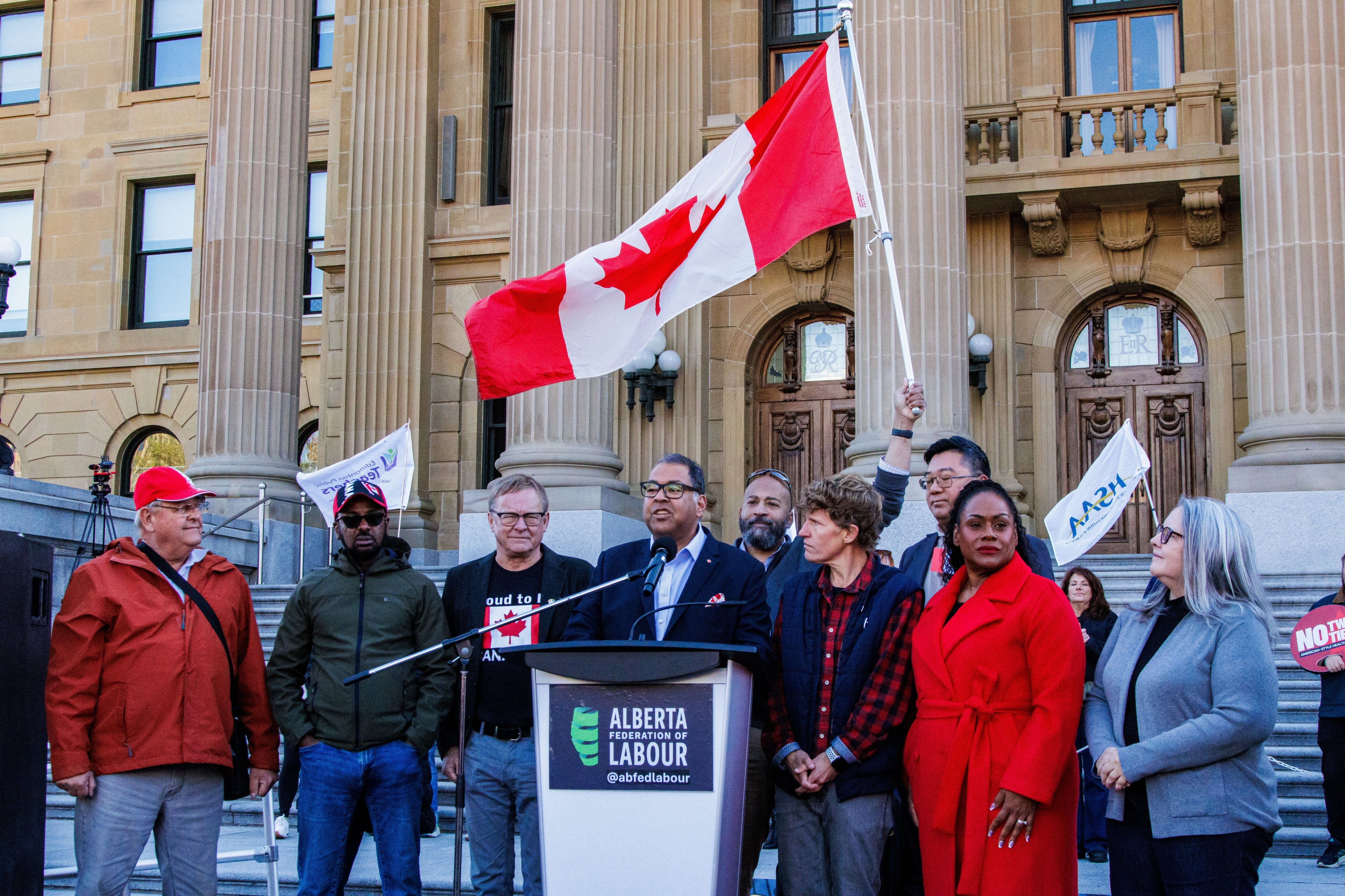 Naheed Nenshi spricht bei einer Kundgebung mit anderen Personen und kanadischer Flagge.
