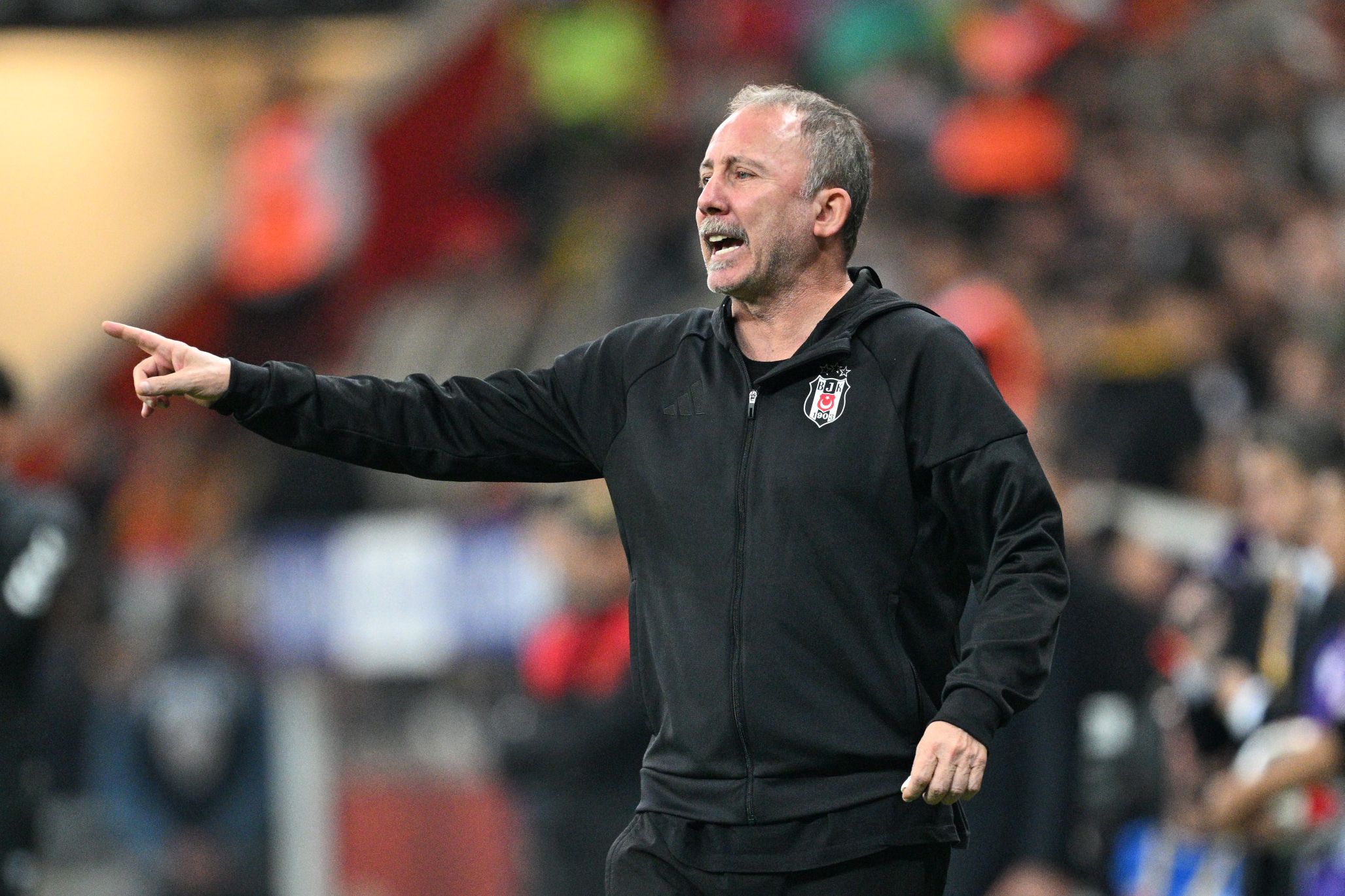 Sergen Yalçın steht in einer schwarzen Trainingsjacke am Spielfeldrand und deutet energisch mit dem Zeigefinger auf das Spielfeld.