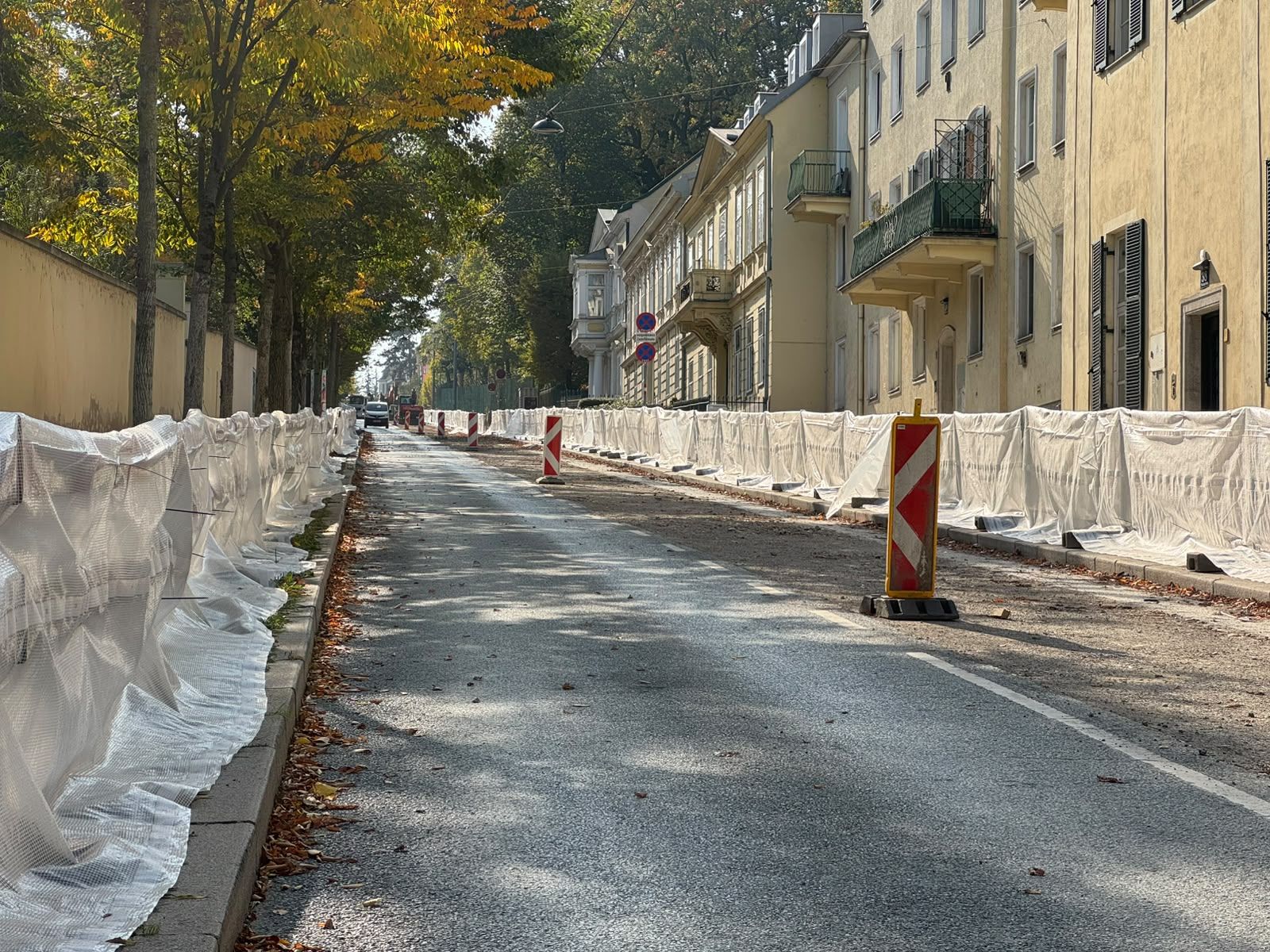 Straße mit Absperrungen und Warnschildern wegen Asbest-Sanierung, Gehwege abgedeckt.