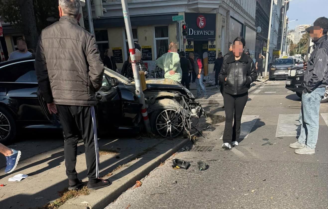 Ein Auto ist nach einem Unfall in Wien Thaliastraße gegen einen Mast gefahren, Menschen stehen daneben.