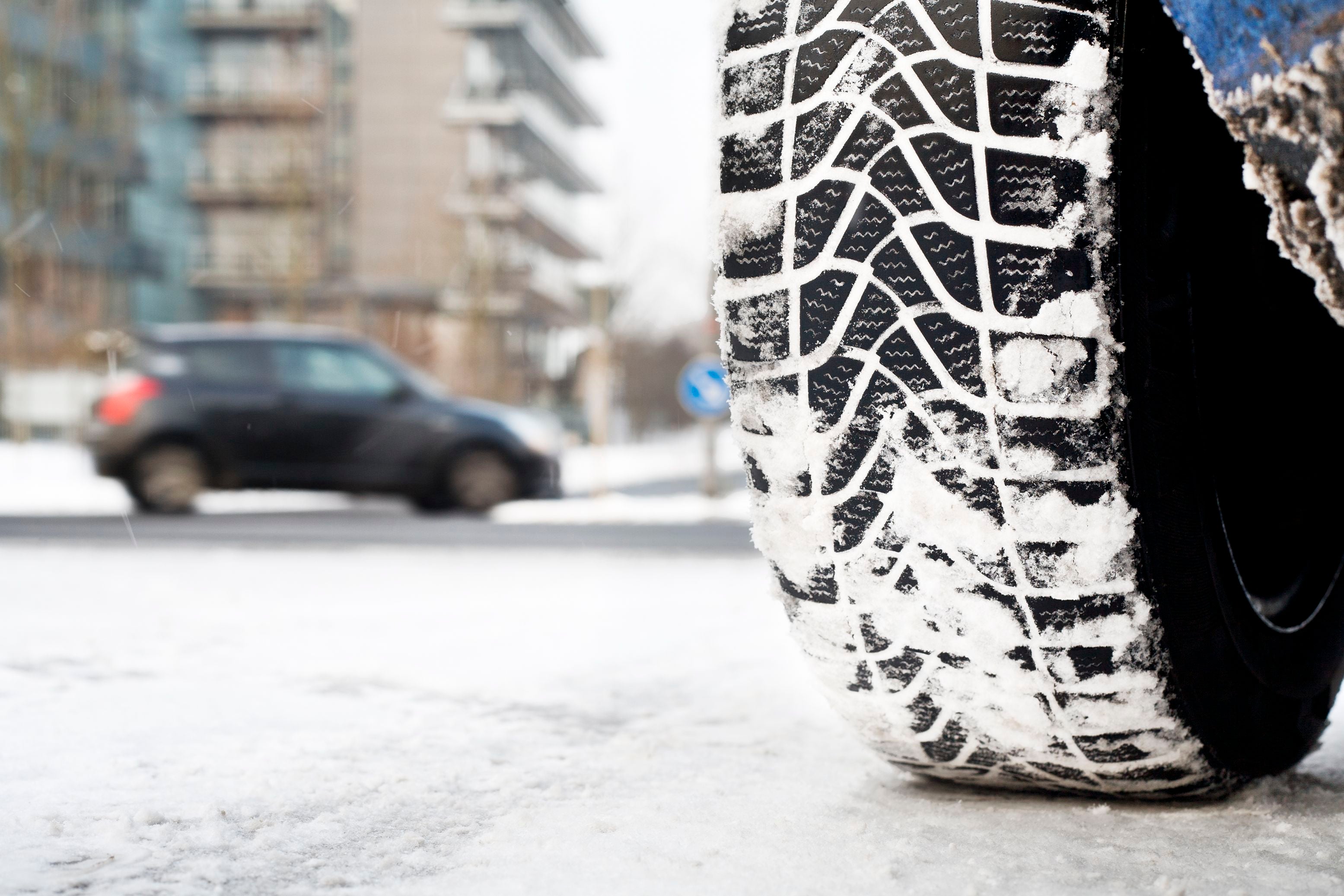 Nahaufnahme eines Autoreifens mit Winterprofil auf schneebedeckter Straße in der Stadt.