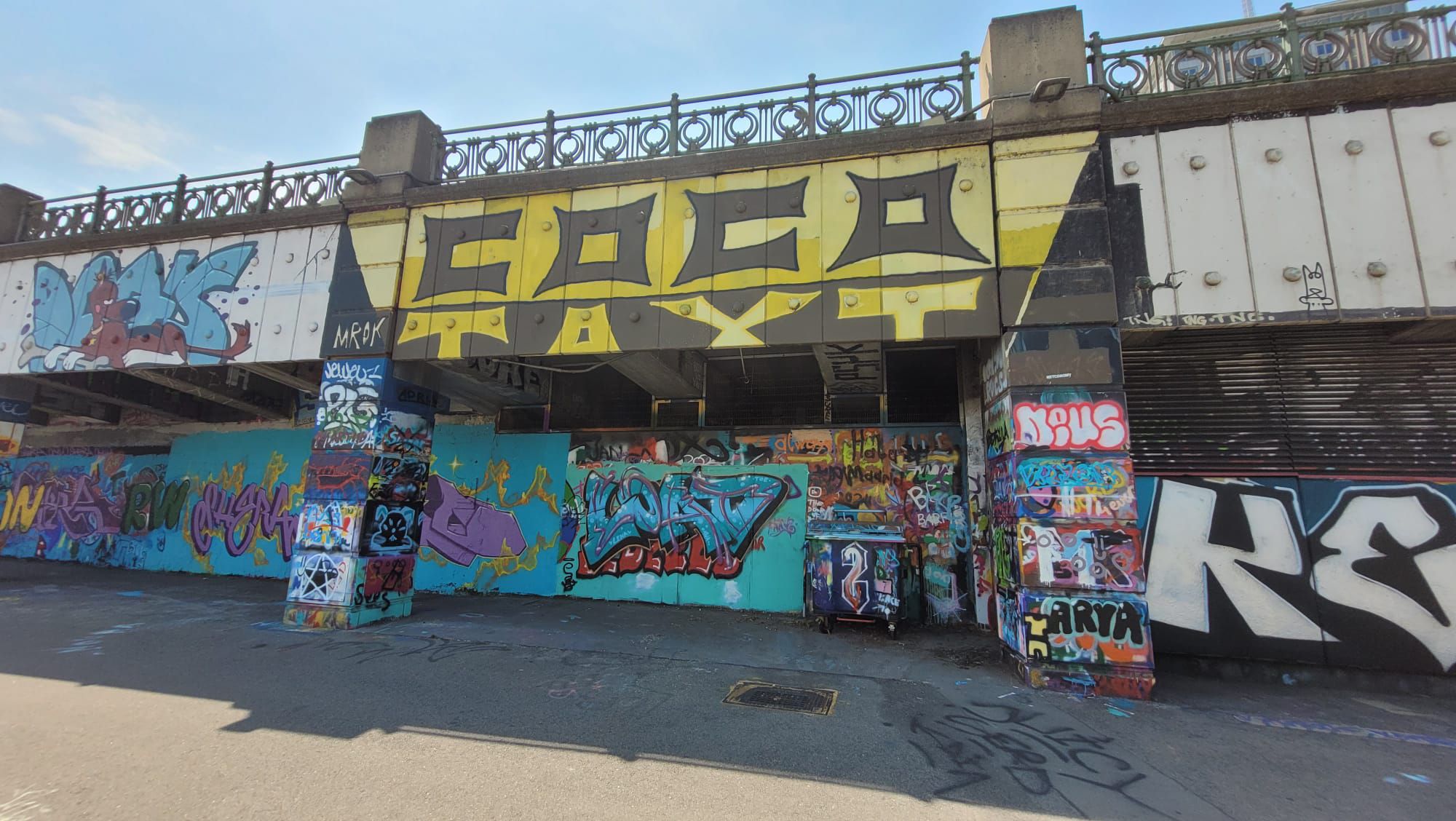 Graffiti mit dem Schriftzug "Coco-Taxi" auf einer Brücke in Wien, bunt besprühte Wände darunter.