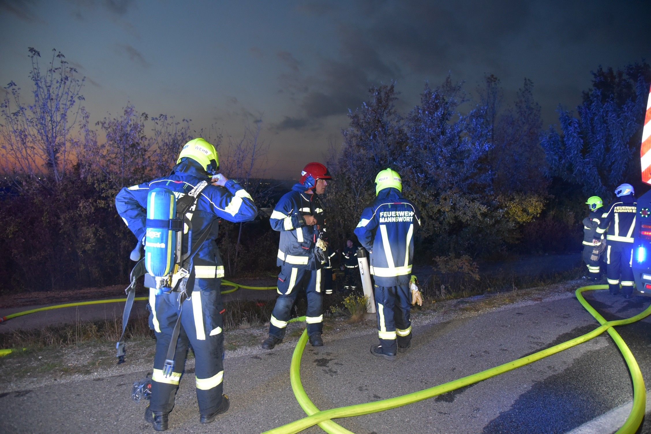 Feuerwehrleute arbeiten abends mit Schläuchen an einer Unfallstelle neben einem entgleisten Zug.