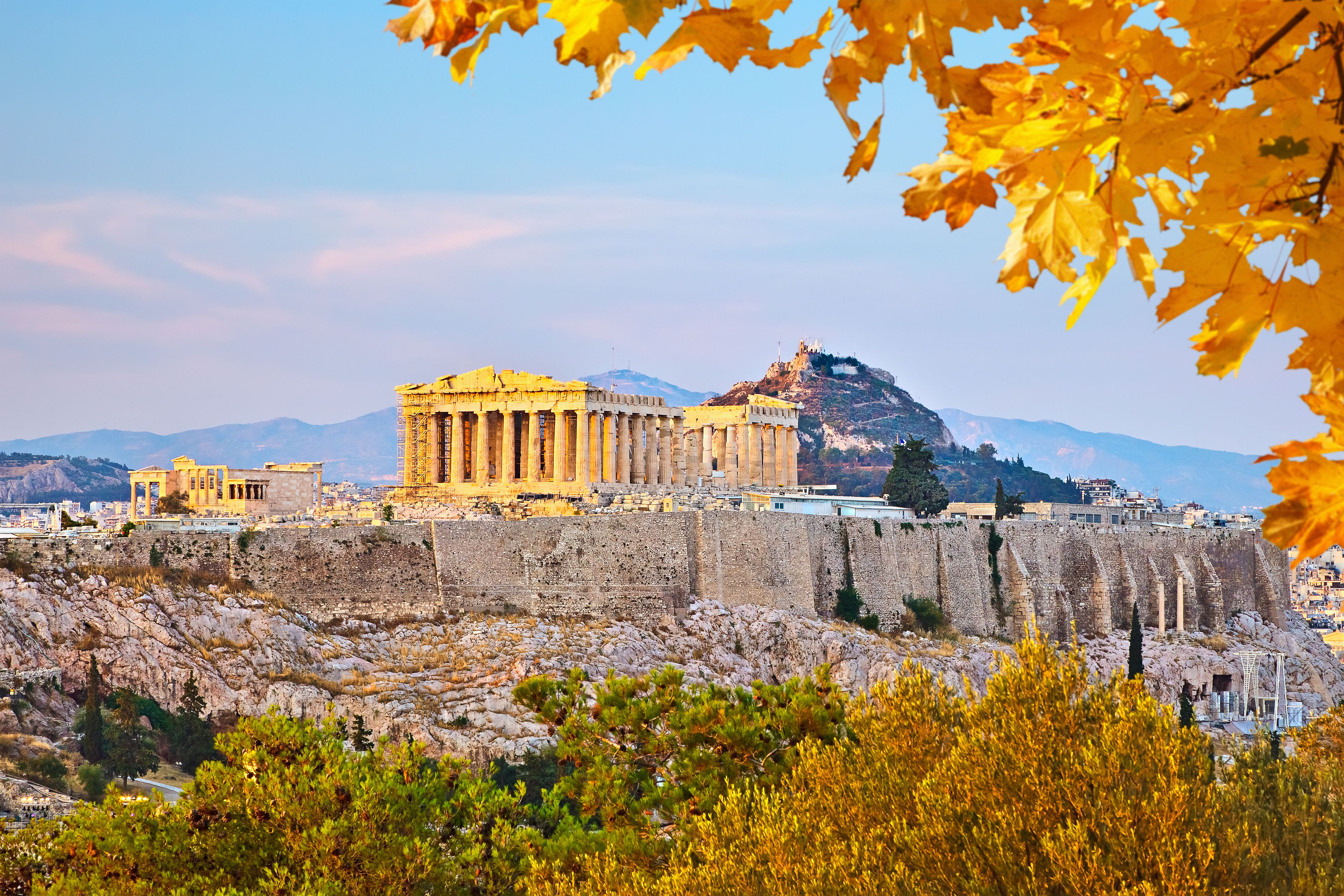 Die Akropolis in Athen bei Sonnenuntergang, umrahmt von herbstlichen Bäumen.