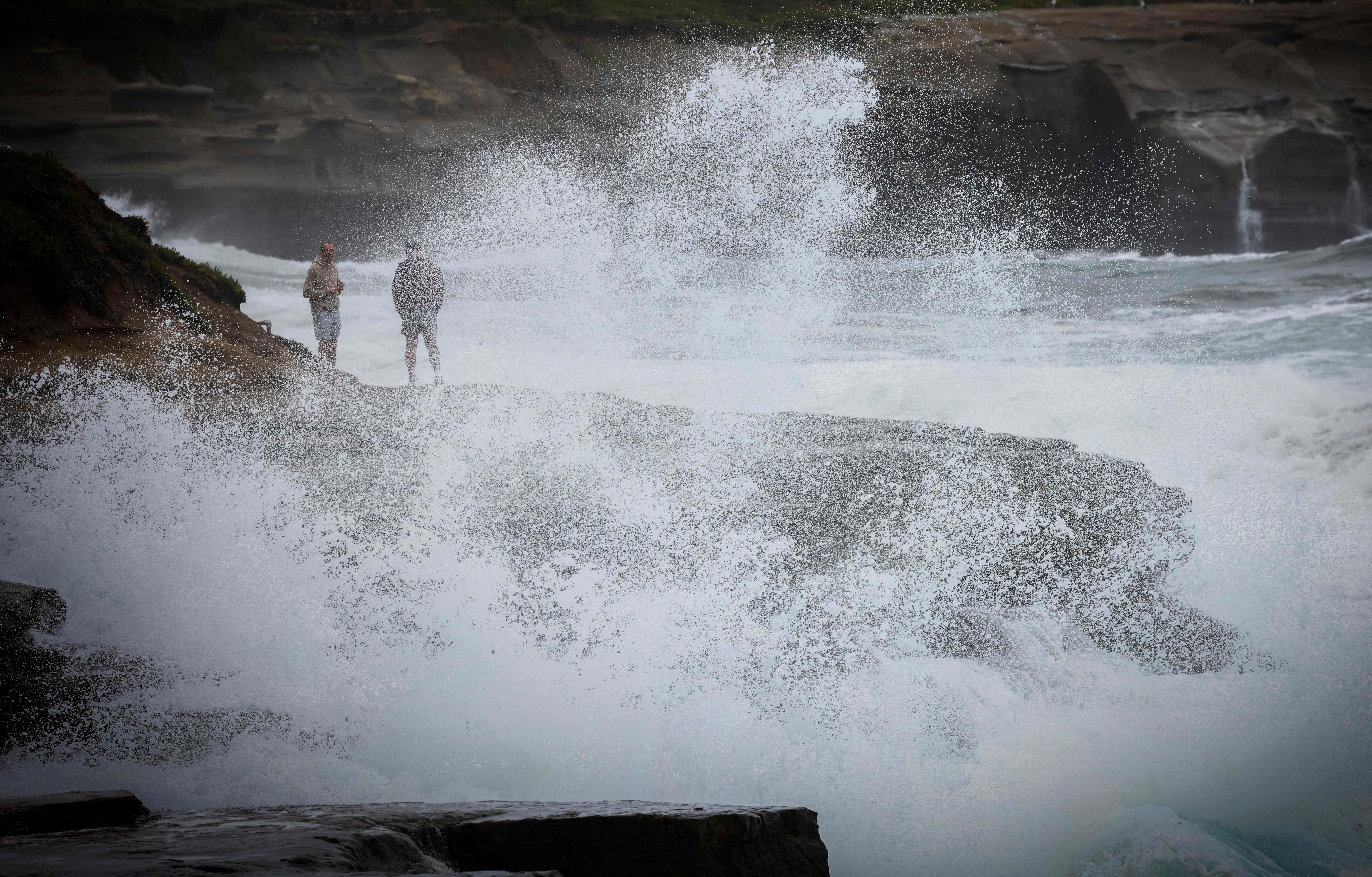 Zwei Personen beobachten, wie große Wellen bei Sturm auf Felsen an der Küste von La Jolla treffen.