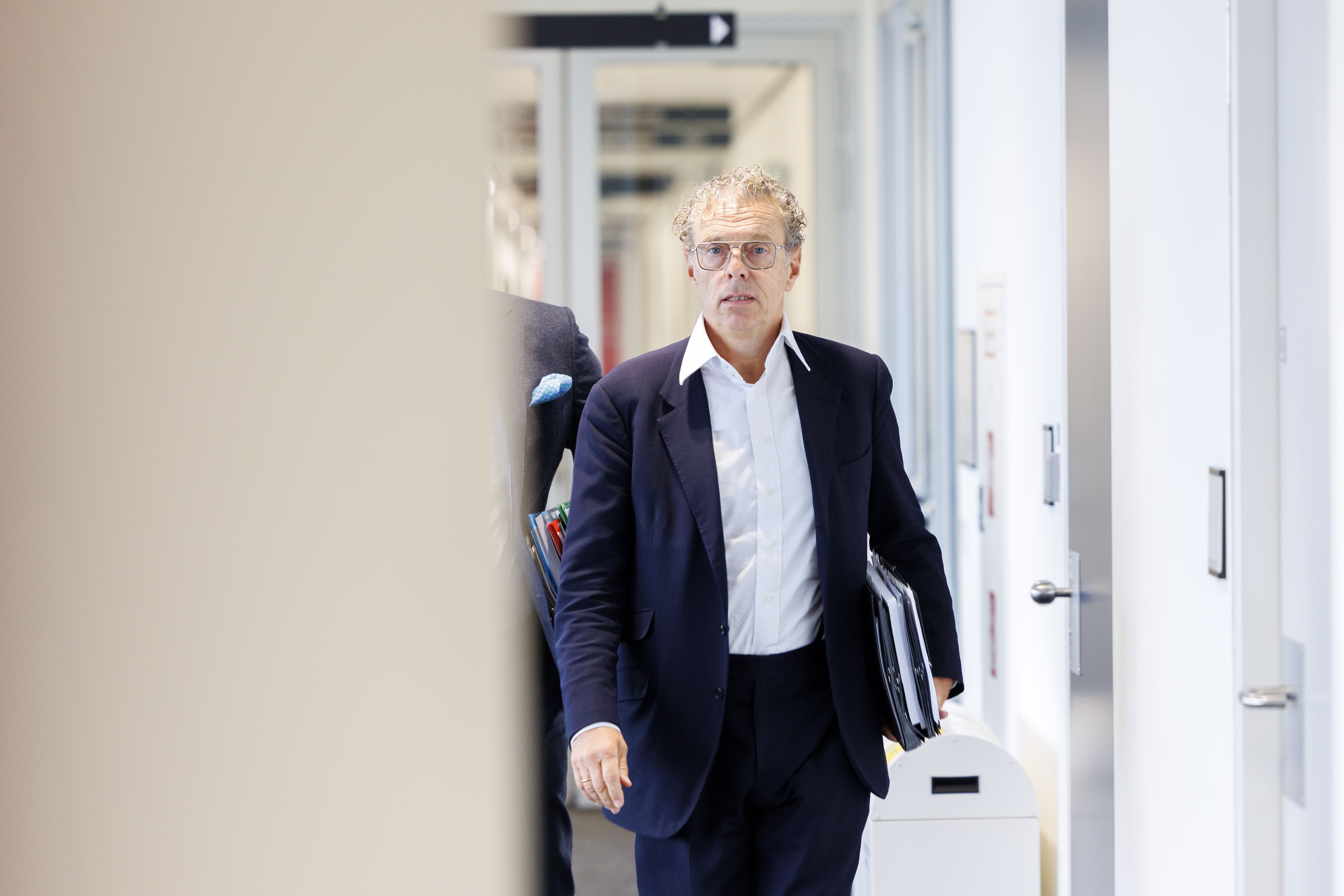 Ein Mann im Anzug mit Unterlagen geht durch einen hellen Flur eines Bürogebäudes.