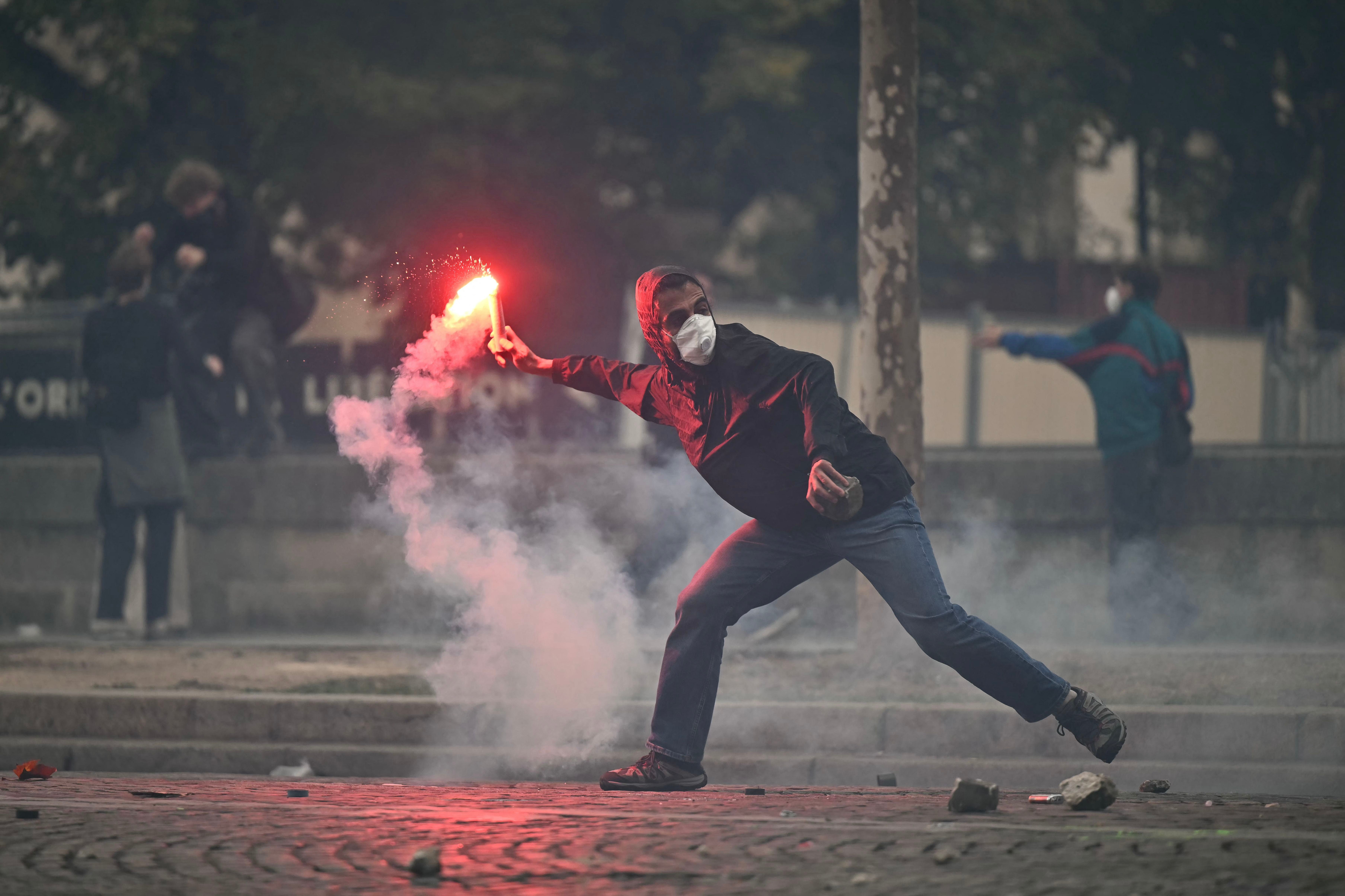 Ein Demonstrant wirft eine Leuchtrakete während eines Protests, Rauch umgibt ihn.