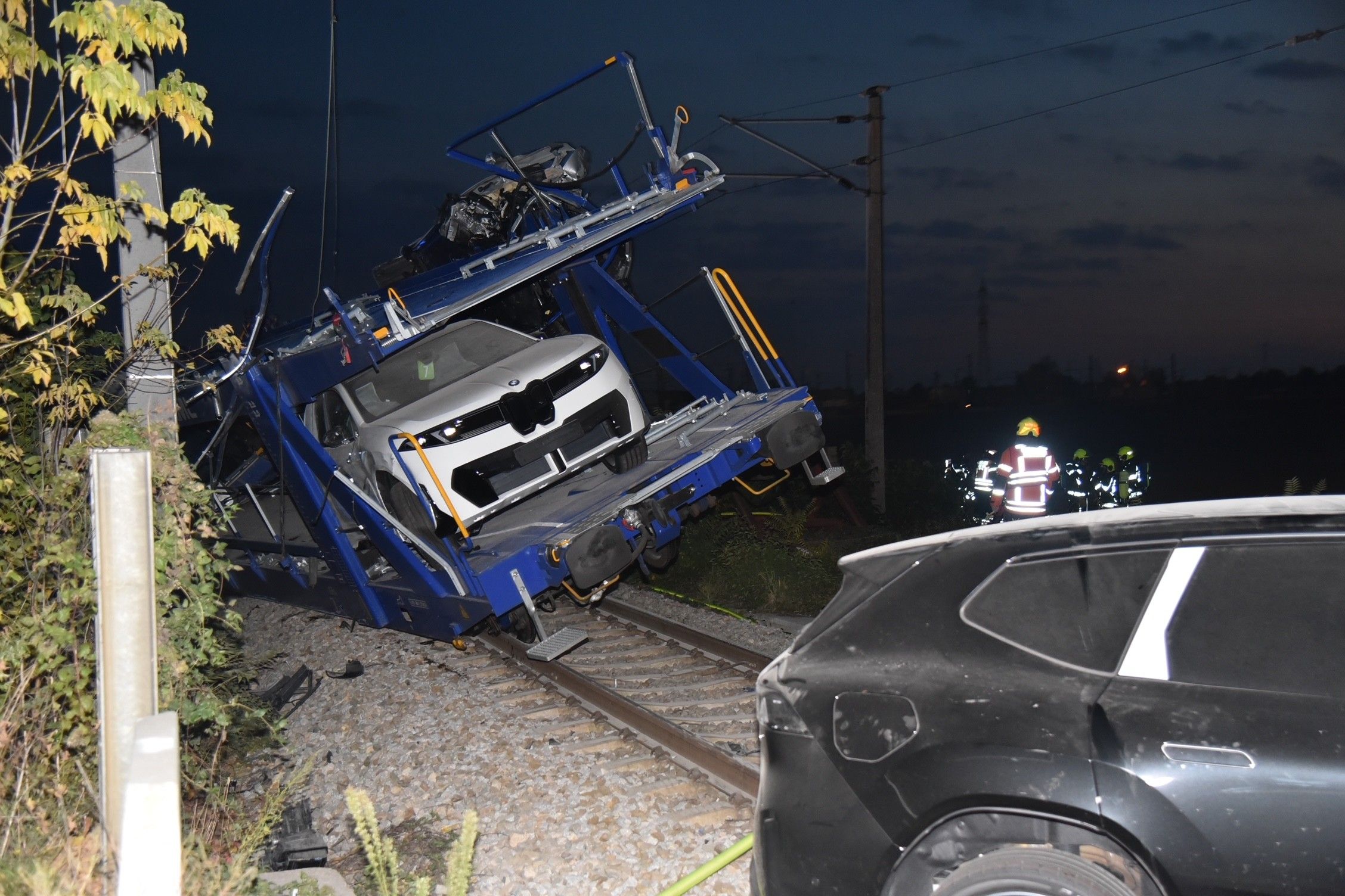 Ein entgleister Autozug mit beschädigten Fahrzeugen und Einsatzkräften bei Nacht.