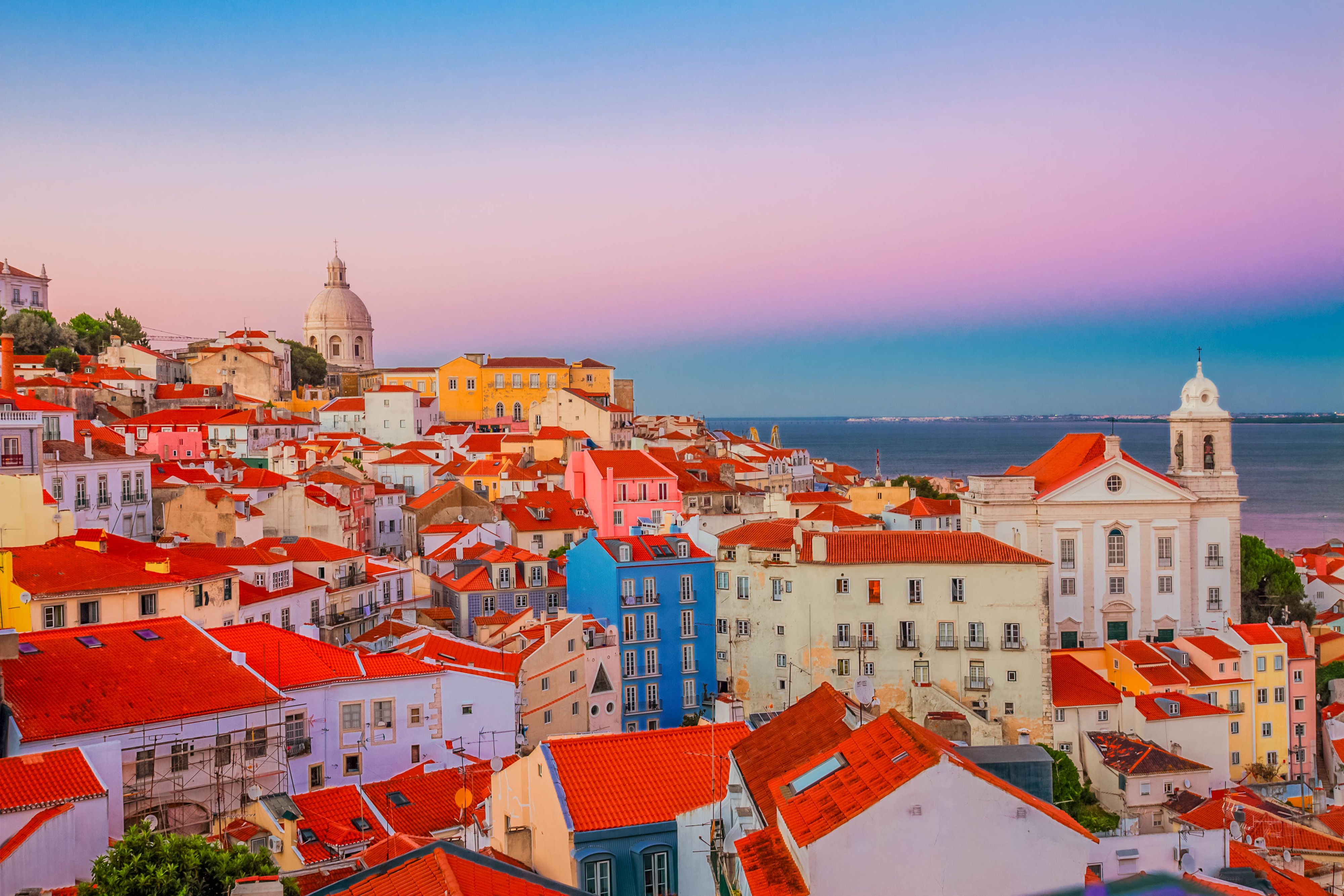 Bunte Häuser mit roten Dächern in Alfama, Lissabon, bei Sonnenuntergang mit Blick aufs Meer.