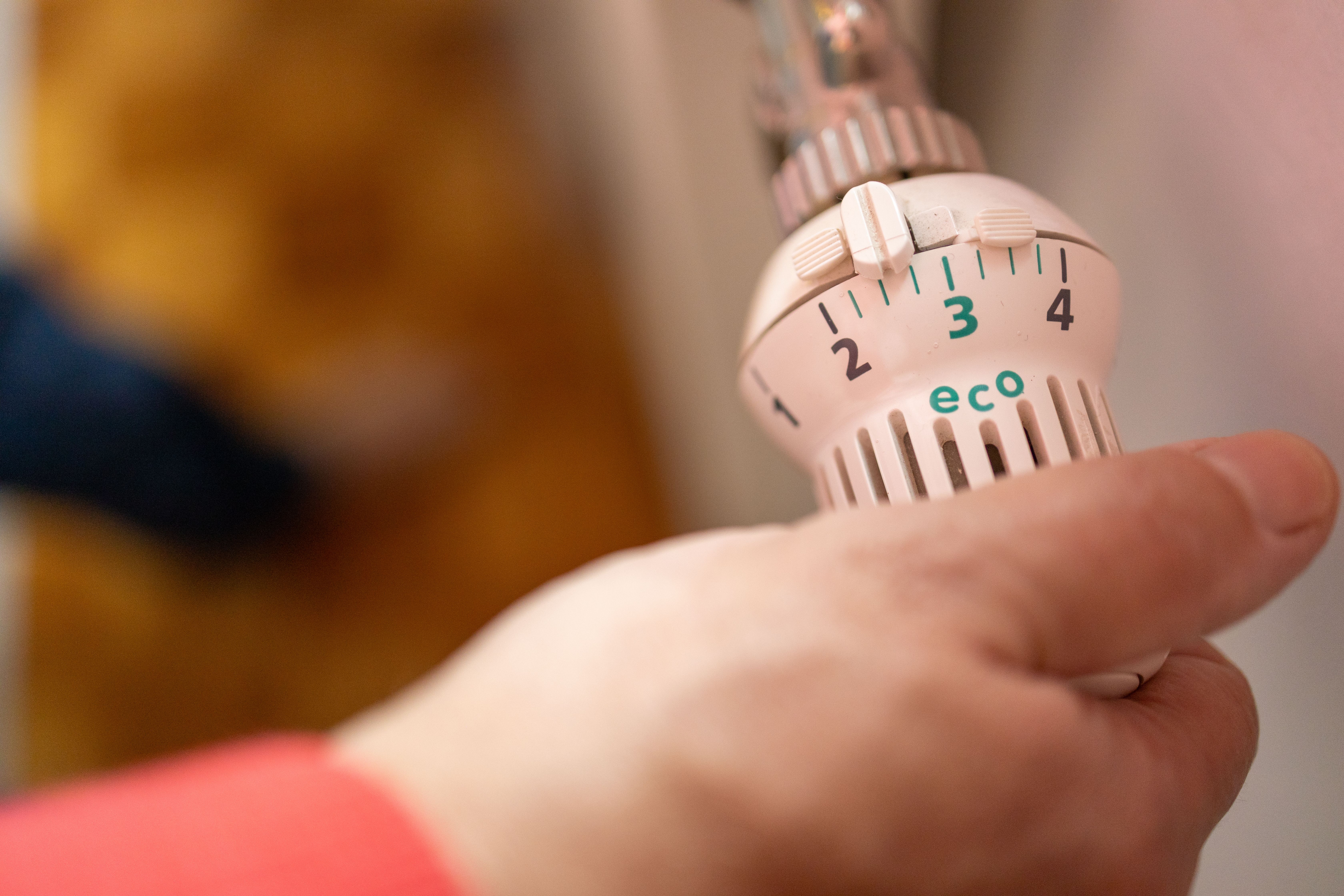 Eine Hand dreht an einem Heizkörper-Thermostat auf die Eco-Stufe.