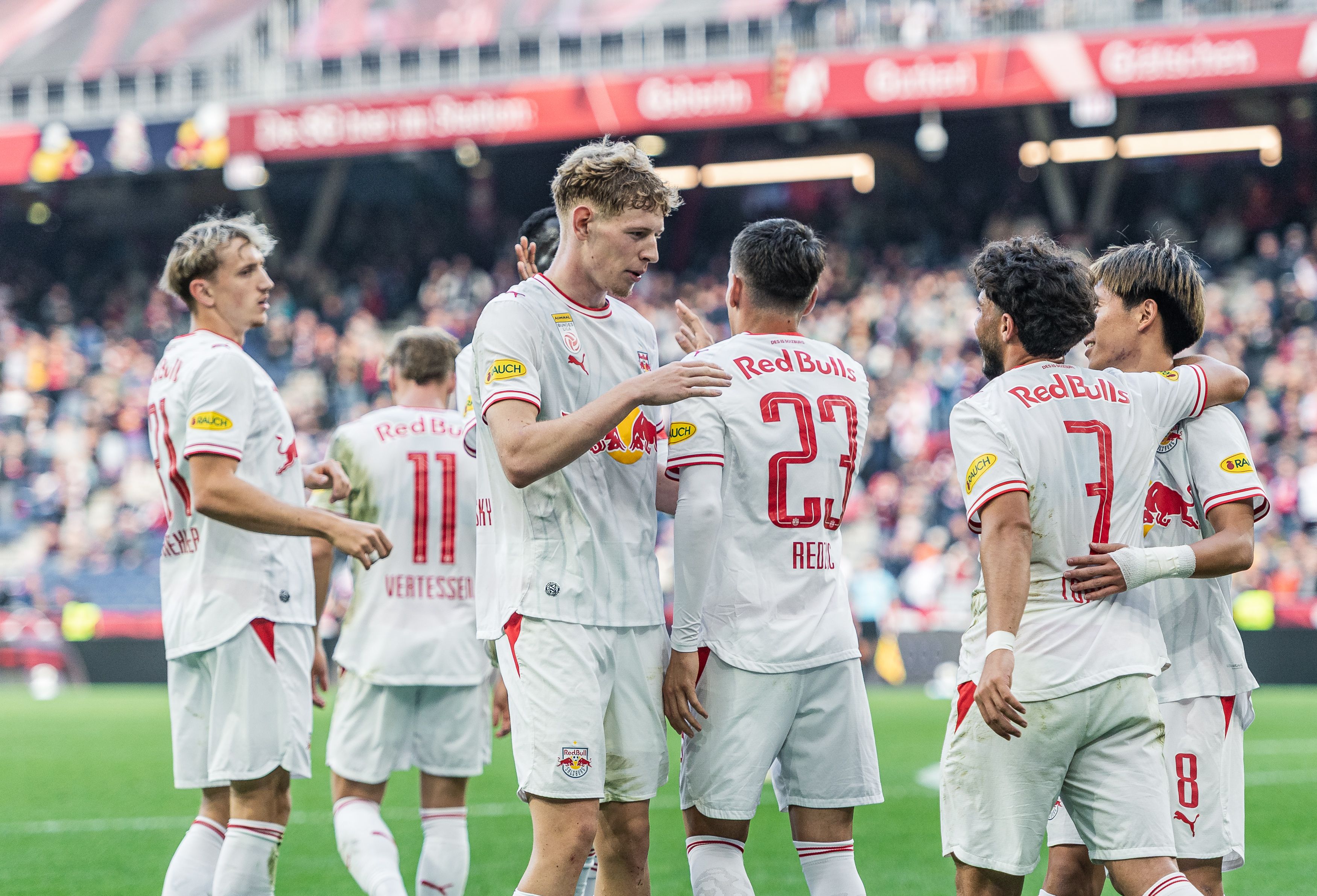 Die Spieler von Red Bull Salzburg klatschen im weißen Trikot auf dem Rasen ab und umarmen sich nach einer erfolgreichen Aktion.