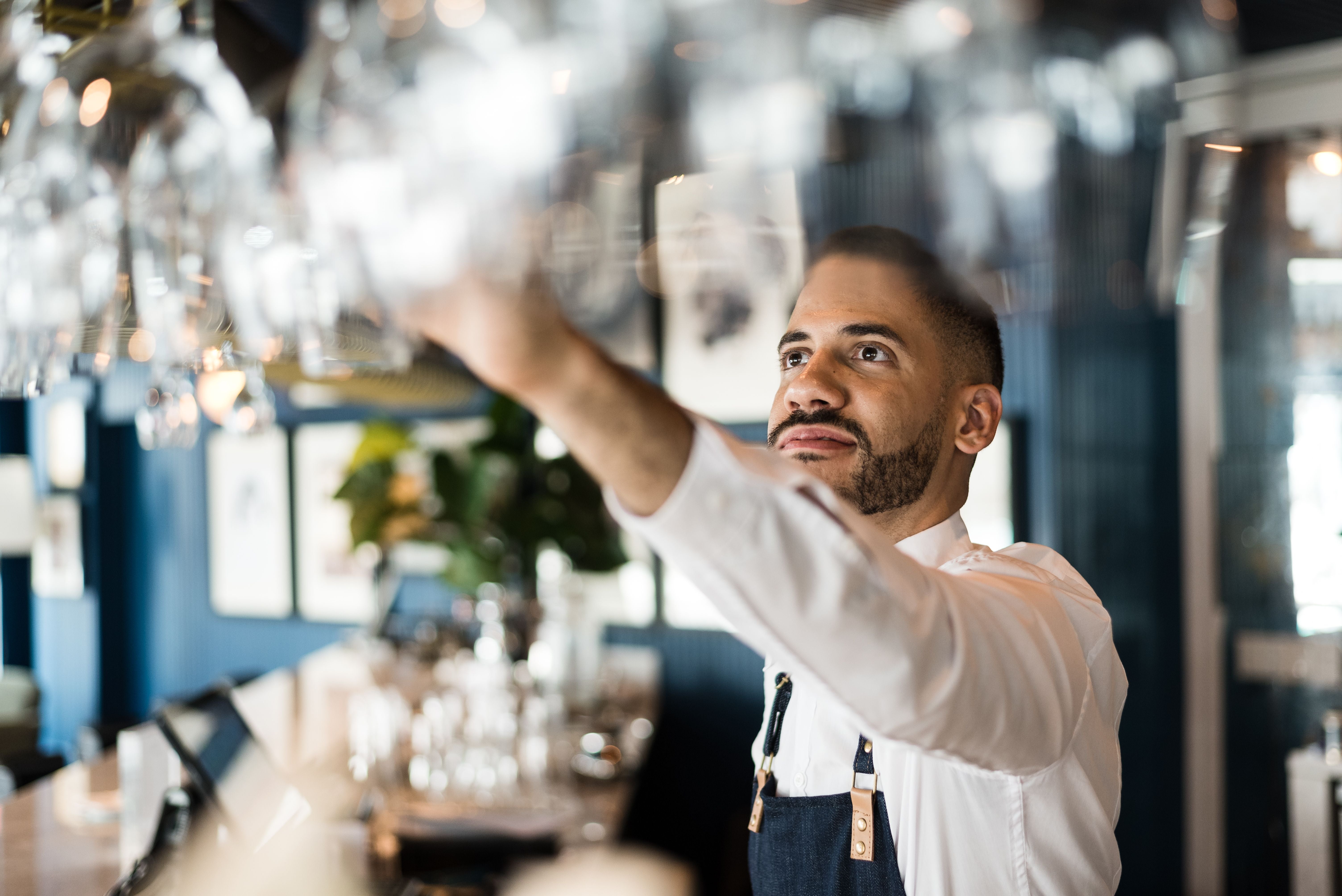 Junger Barkeeper mit Bart ordnet Gläser über einer Theke in einer Bar.