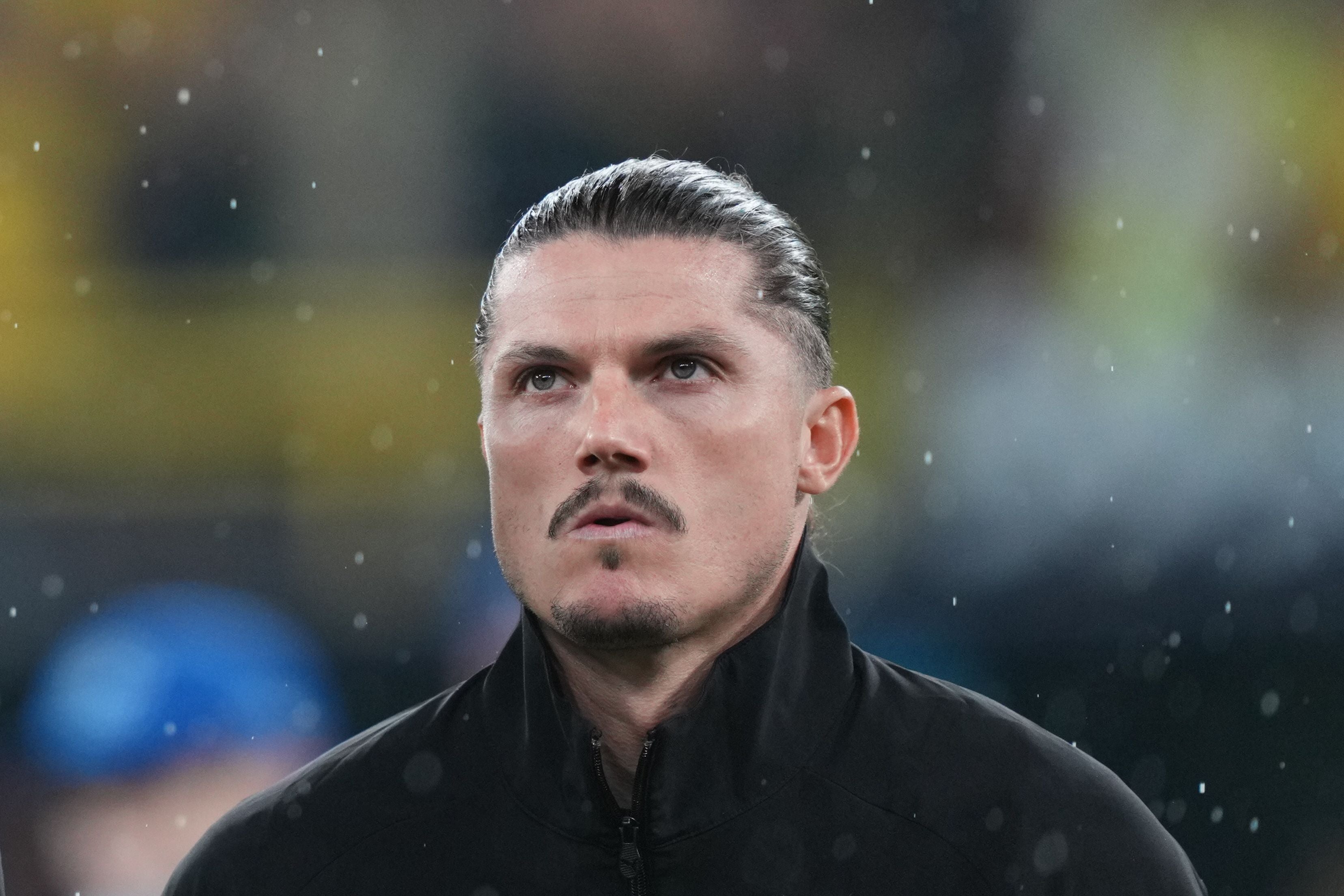 Ein Mann mit zurückgekämmten Haaren steht im Regen und blickt nach oben.