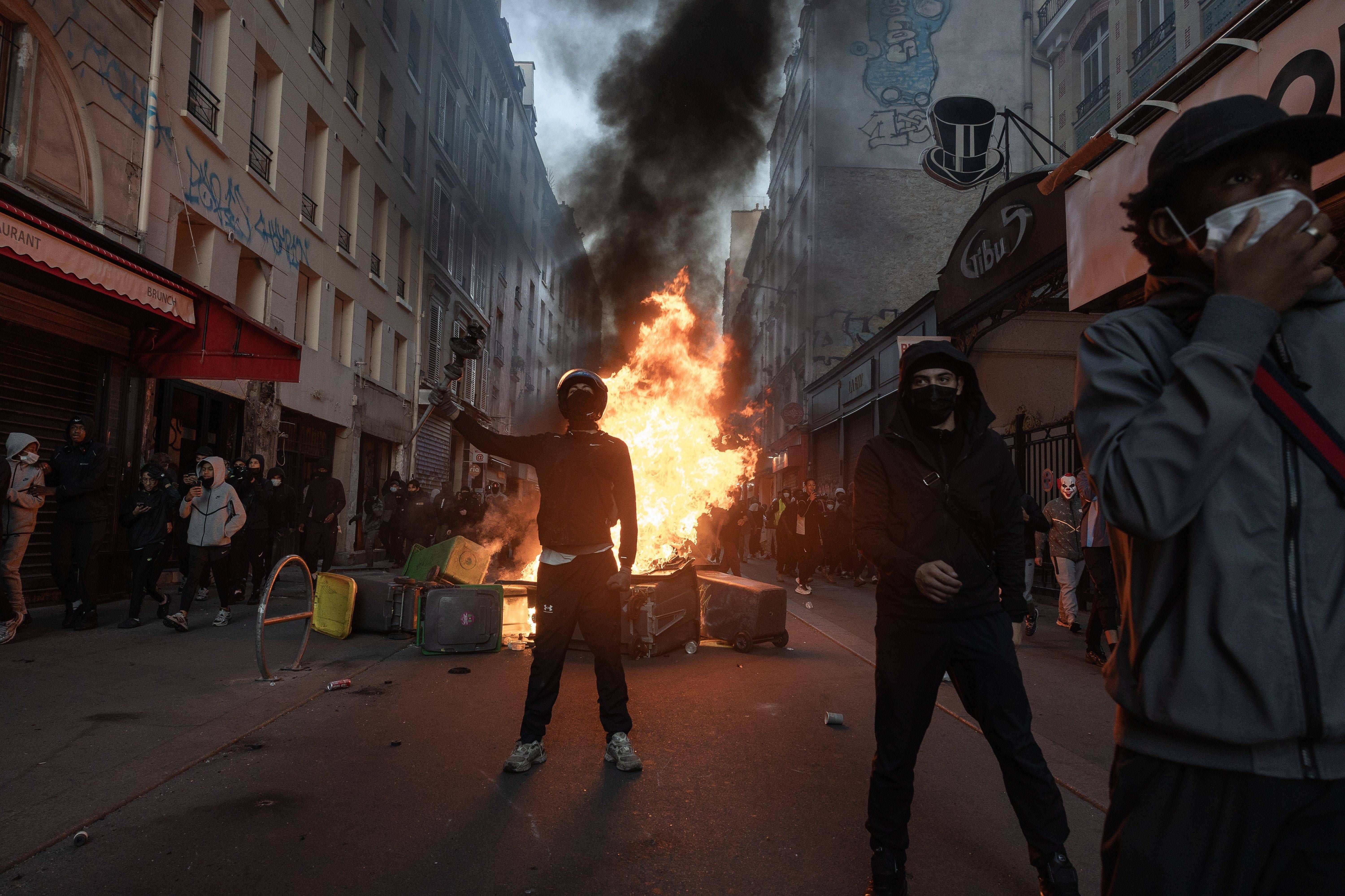 Protestierende vor brennender Barrikade in einer Straße in Paris, viele tragen Masken.