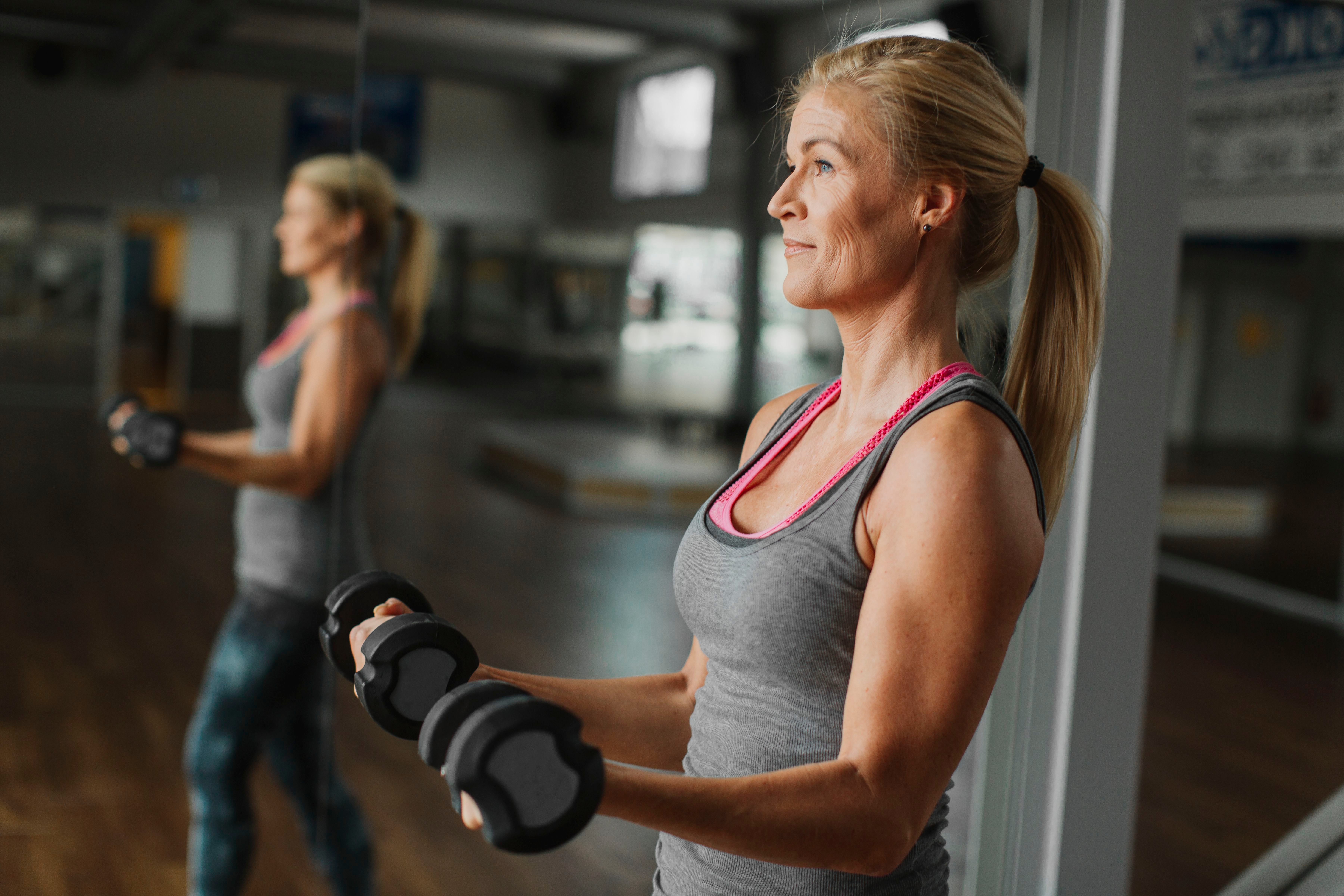Frau trainiert im Fitnessstudio mit Kurzhanteln vor einem Spiegel.