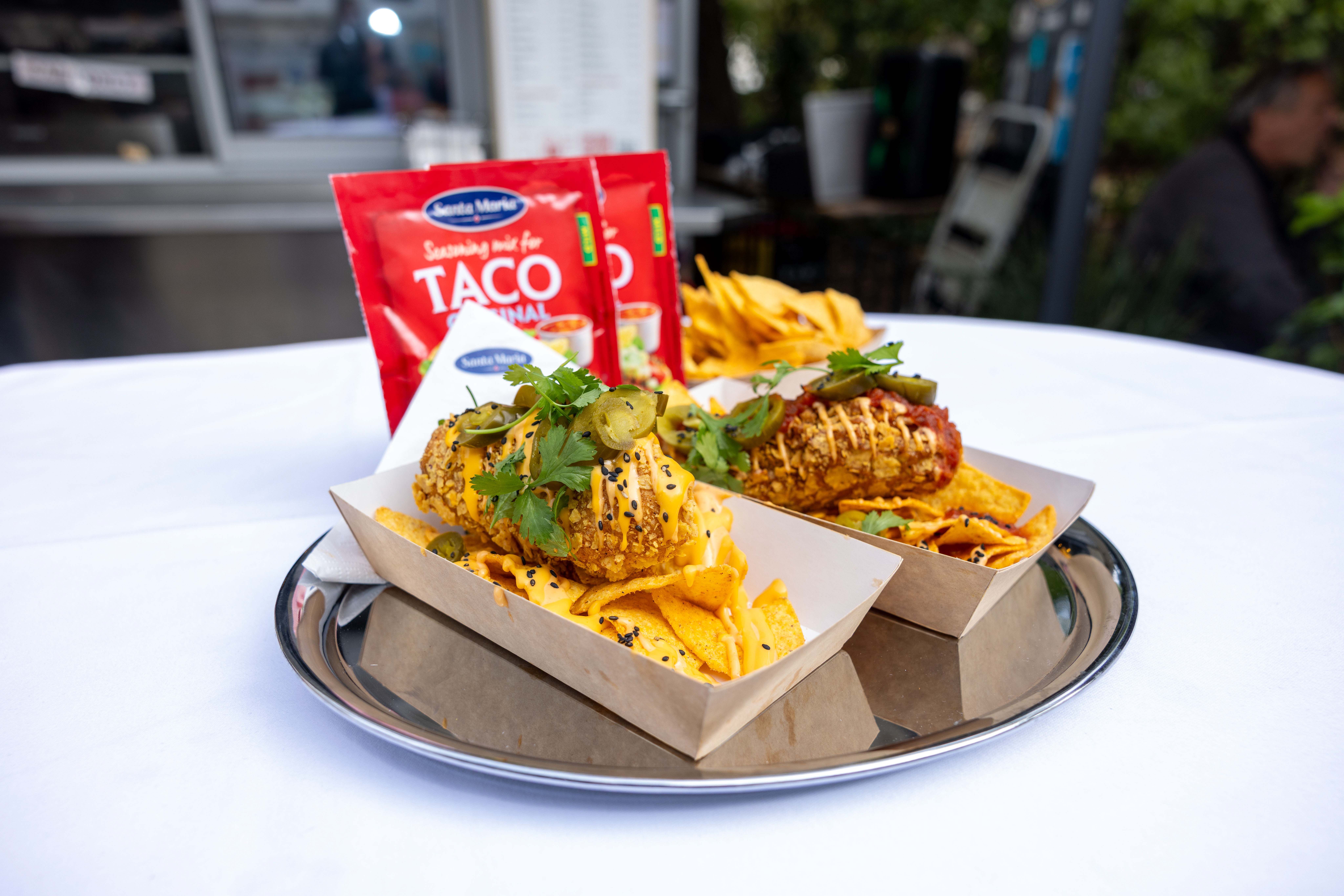 Zwei Wiener Nacho Dogs mit Nachos und Saucen auf einem Tablett, daneben Taco-Gewürzmischung.