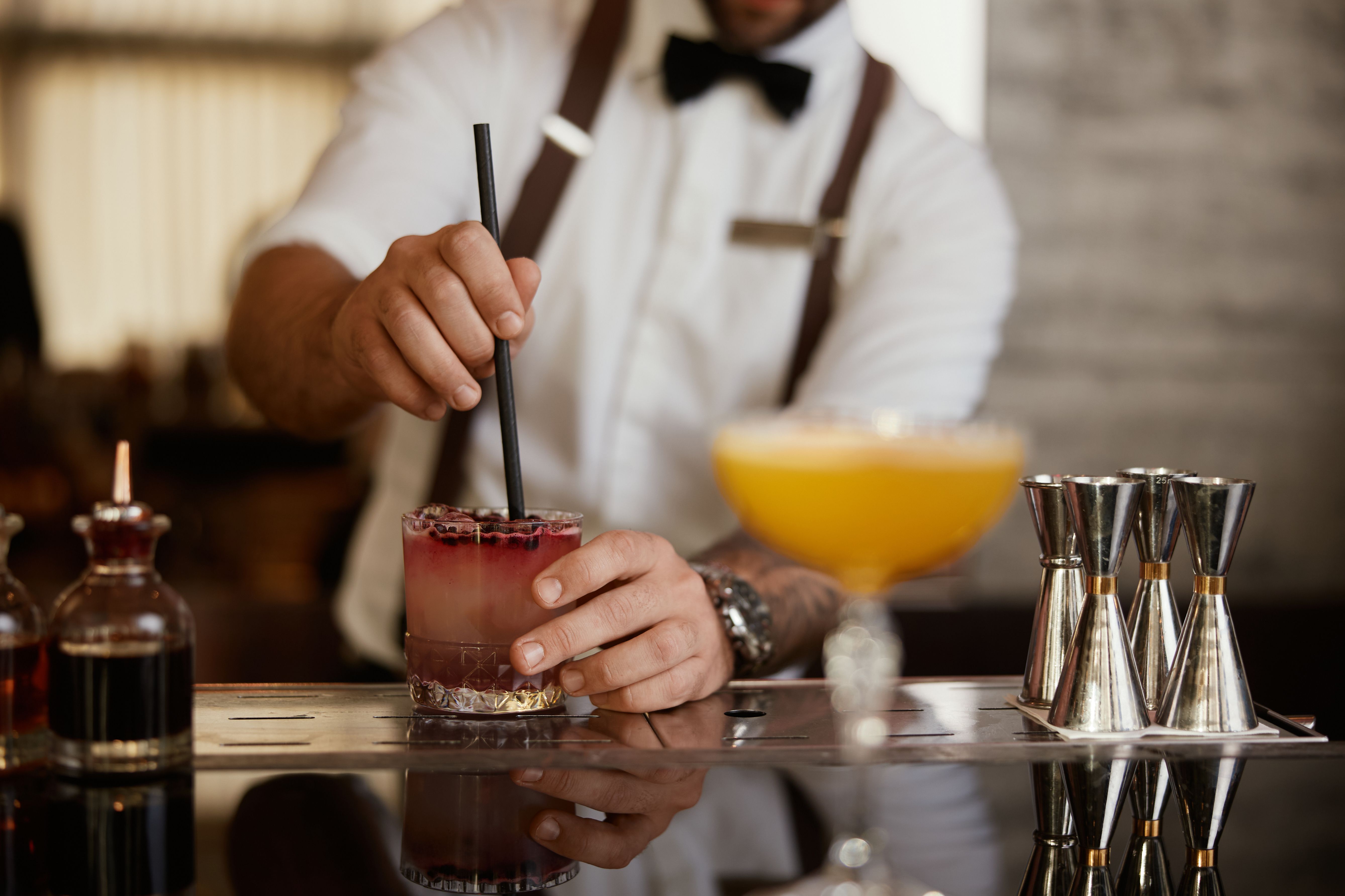 Barkeeper rührt einen Beeren-Cocktail mit einem Strohhalm an einer eleganten Bar um.